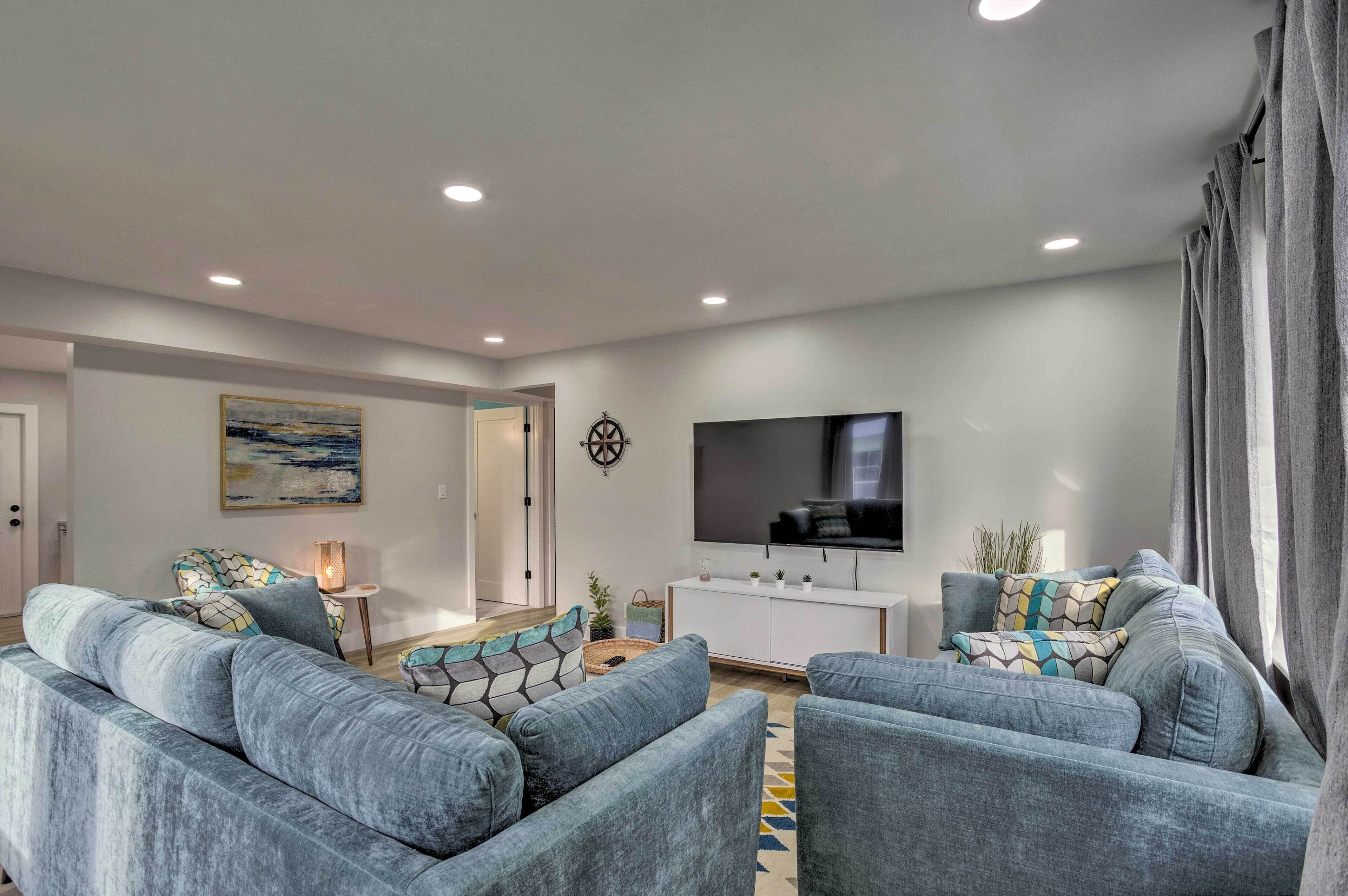 A modern living room with grey sofas, a flat-screen TV, a white cabinet, and a painting on the wall.