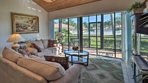 A spacious living room with a large window, a ceiling fan, and a painting on the wall.