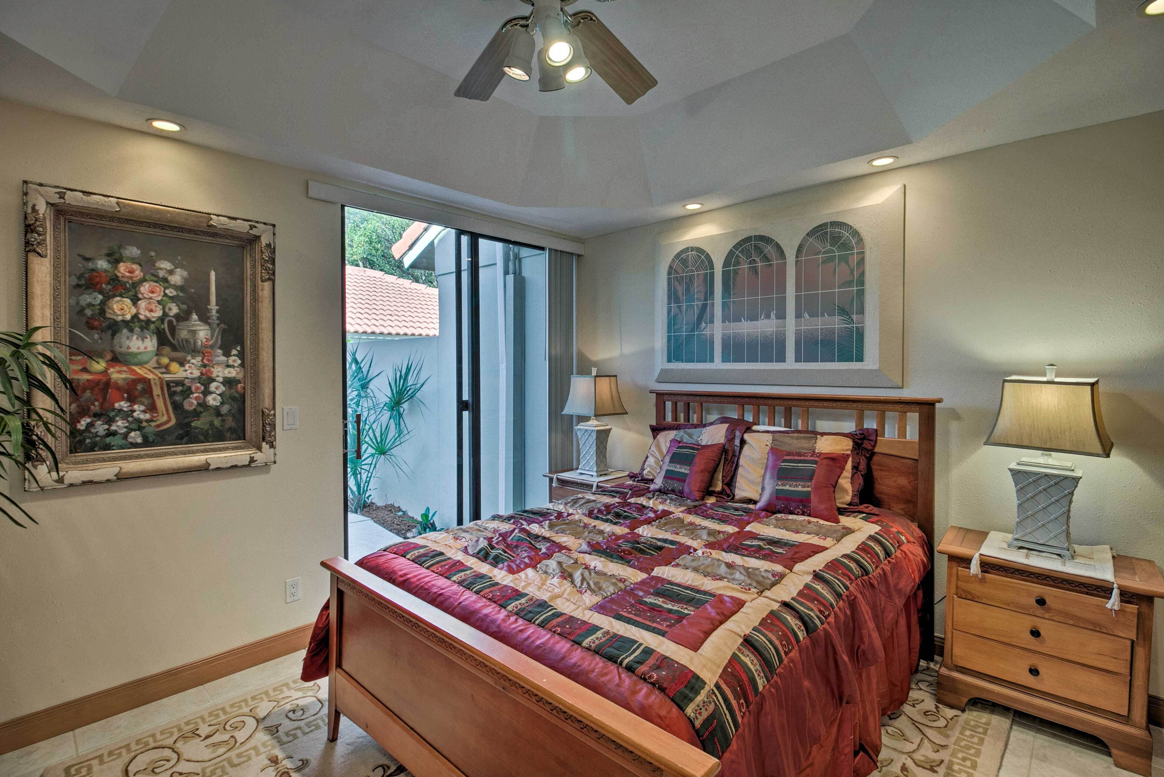 A bedroom with a large bed, a nightstand, a dresser, a ceiling fan, and a window with a view of the outside.