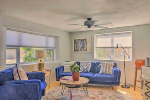 Un salon avec un canapé bleu, une table basse ronde ornée d’une plante et un ventilateur de plafond.