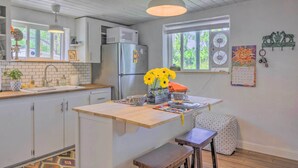 Una cocina con armarios blancos, encimera de madera, un refrigerador, un microondas y una ventana con vistas a zonas verdes.