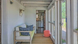 Un pasillo estrecho con una cama, un reposapiés rojo y una cocina visible a través de una puerta abierta.
