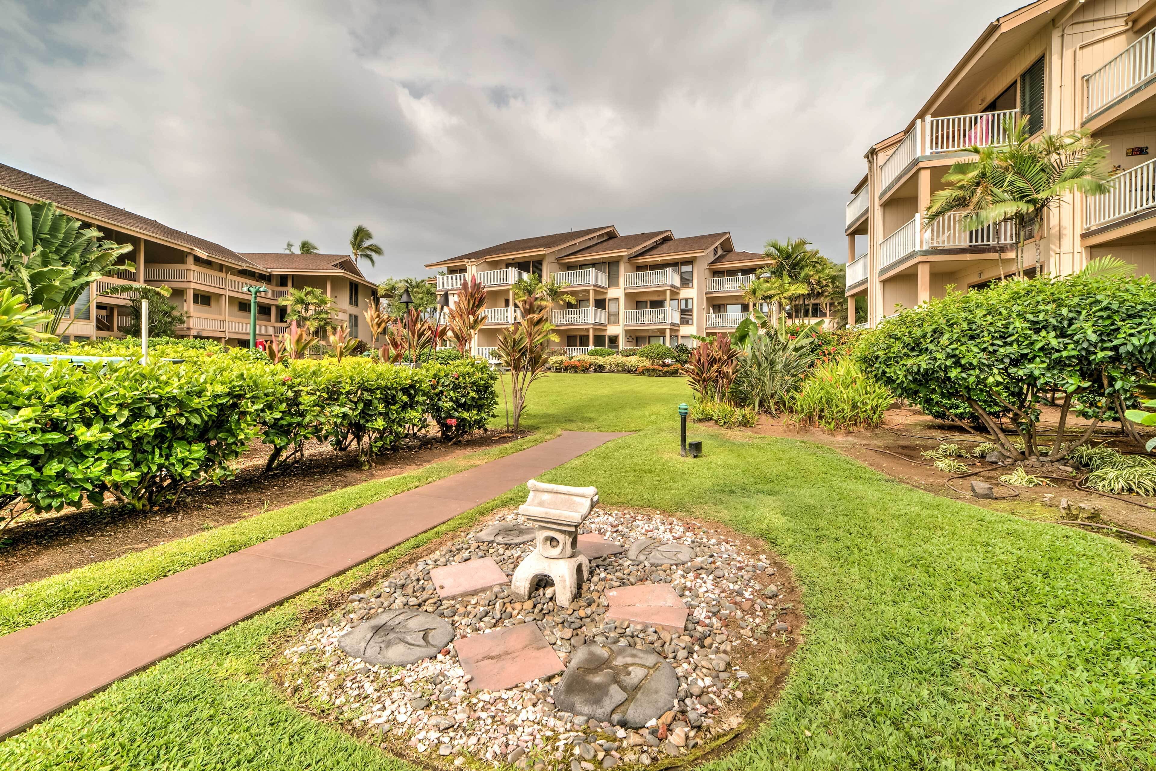 A hotel with multiple balconies, a well-maintained garden with a central seating area, and a pathway leading to the building.