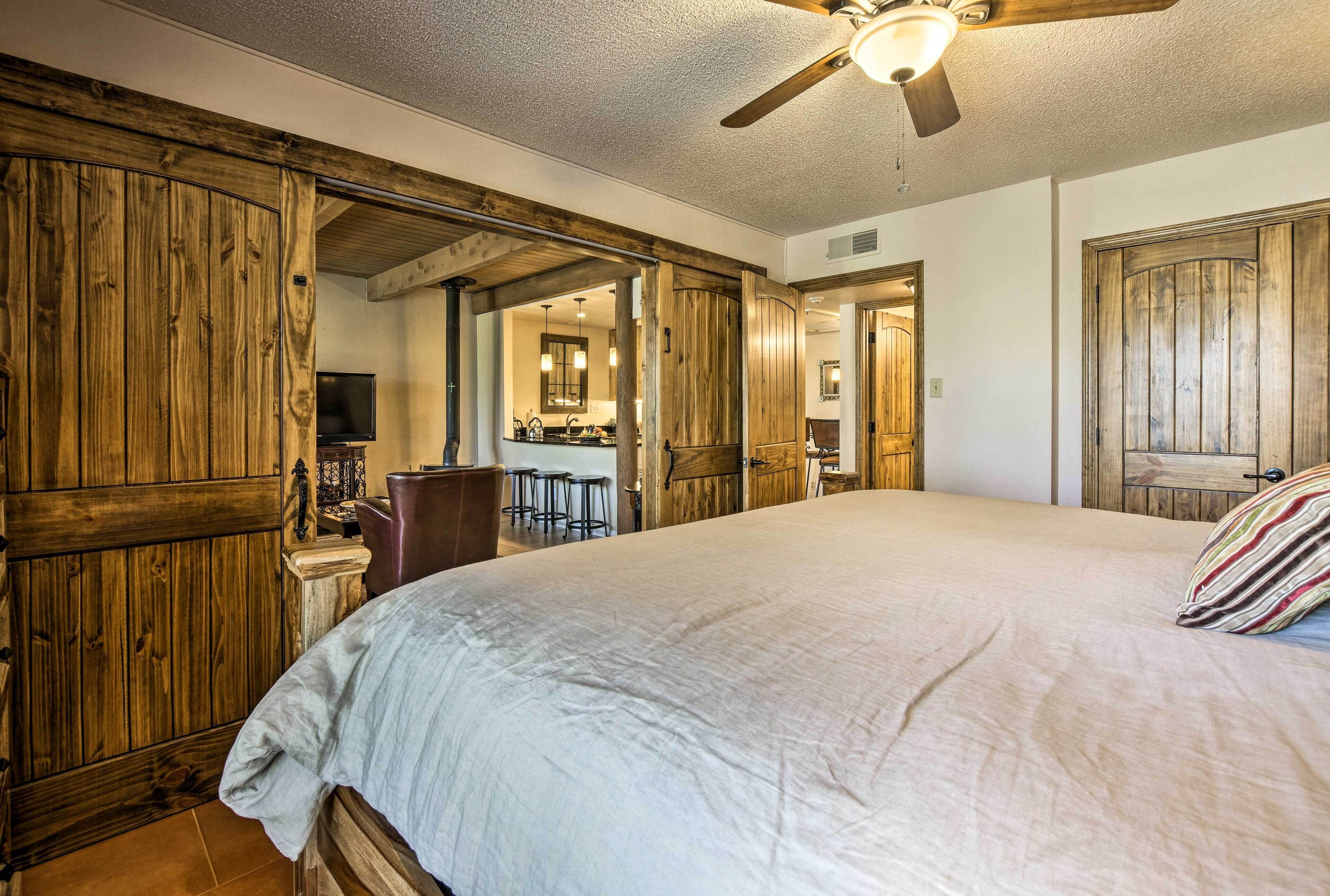 A bedroom with a large bed, wooden walls, a ceiling fan, and a view into the bathroom.