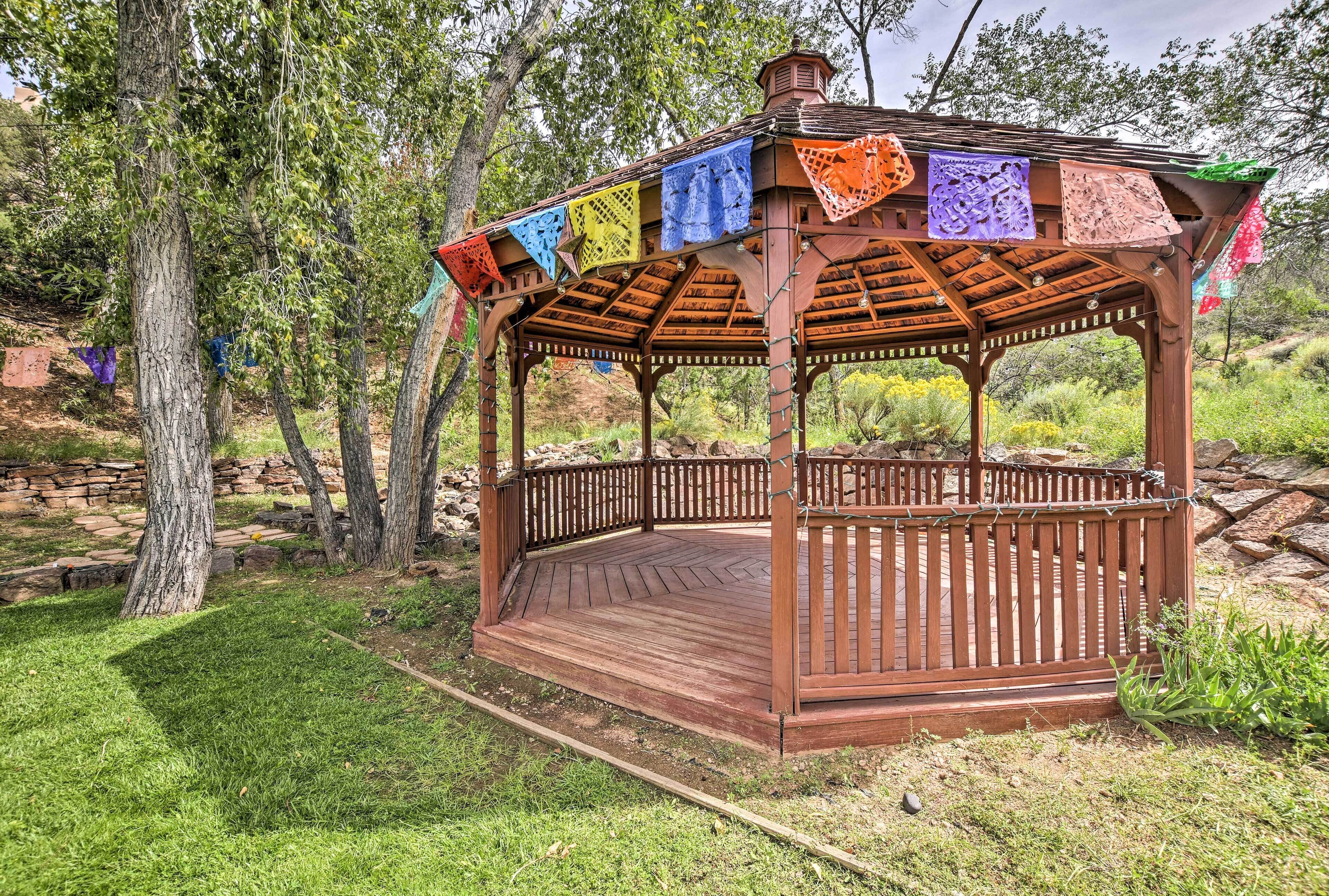 A wooden gazebo with a circular floor and a roof supported by wooden beams.