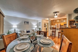 A dining area with a round table set for four, surrounded by wooden chairs. There is a kitchen area with wooden cabinets and a countertop visible in the background.