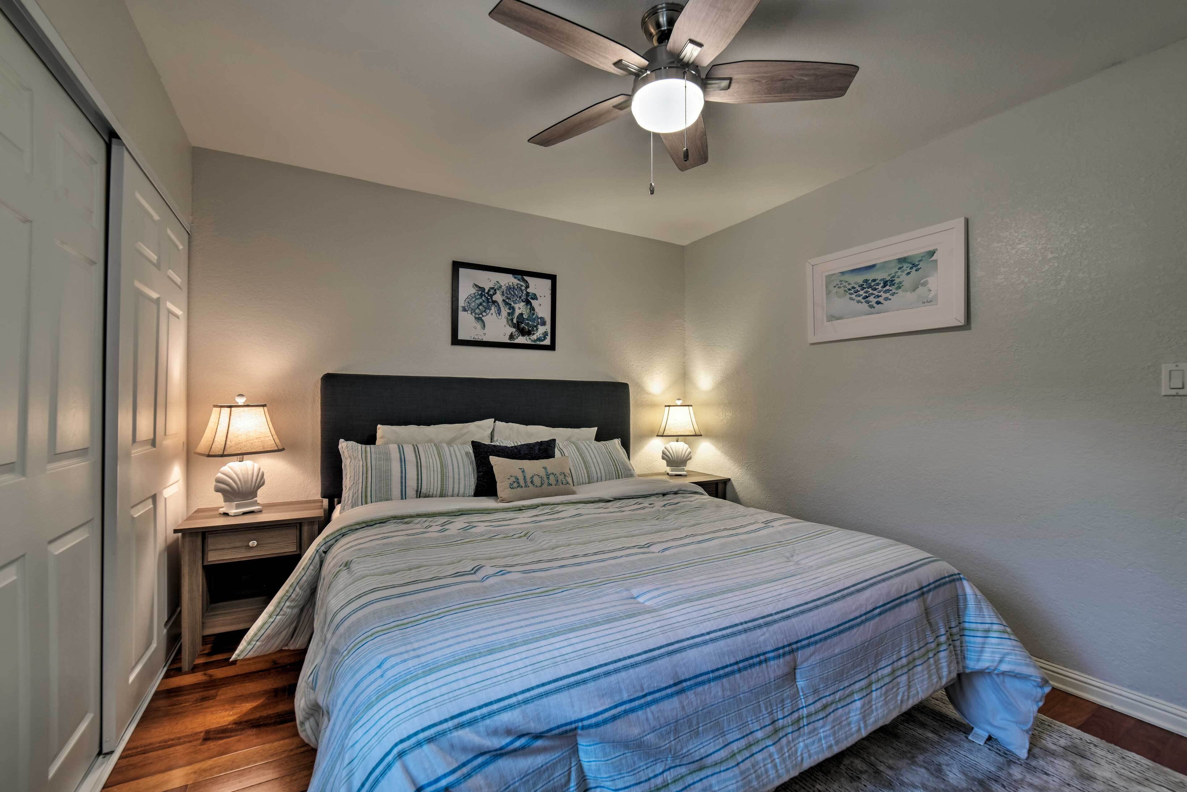 A bedroom with a bed, two bedside tables with lamps, a ceiling fan, and two framed artworks on the wall.