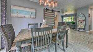 Uma área de refeições com mesa e cadeiras de madeira, luminária pendente e quadro com pássaros na parede.