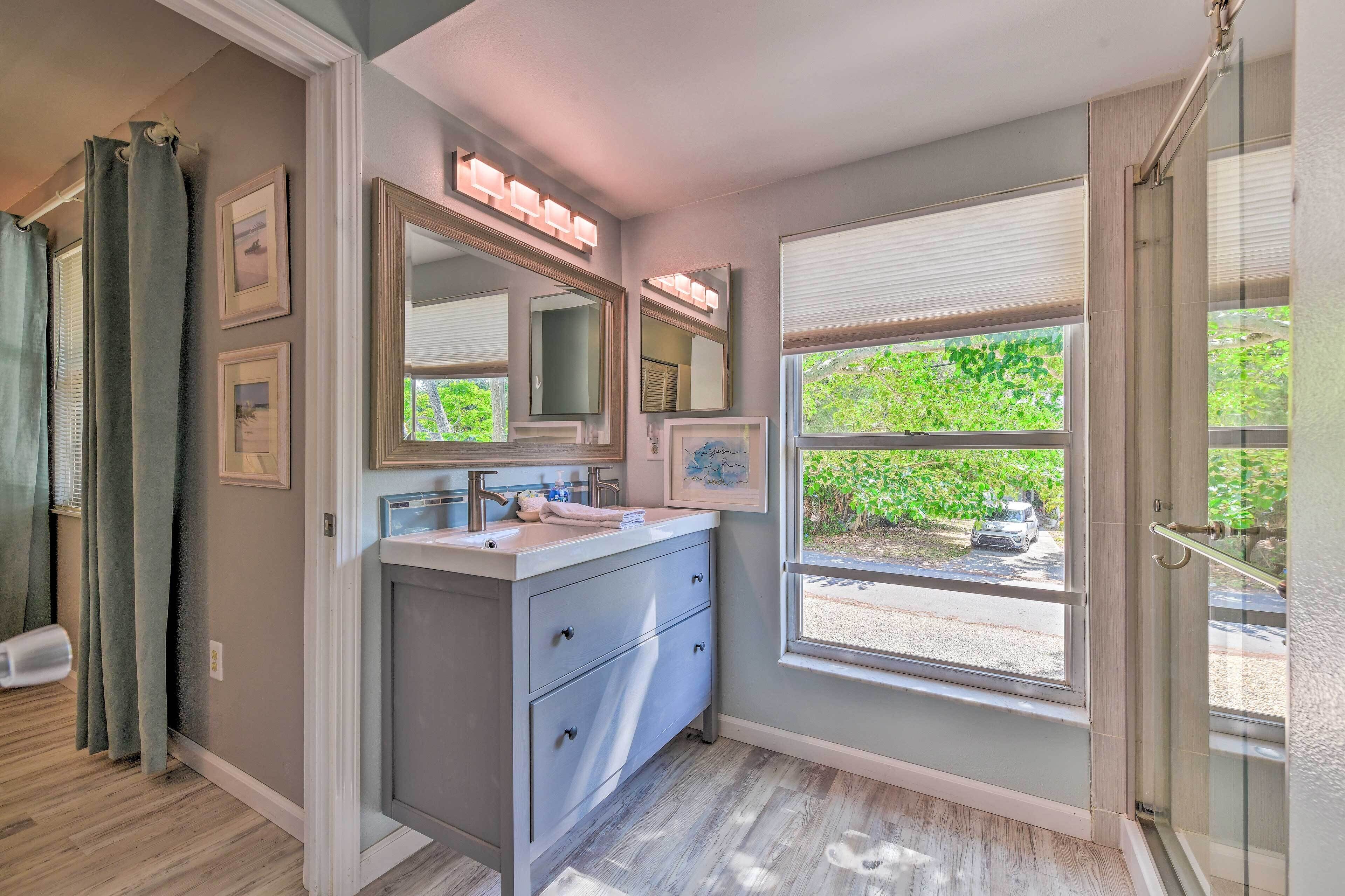 A bathroom with a vanity, mirrors, and a window with a view of greenery and a parked car.