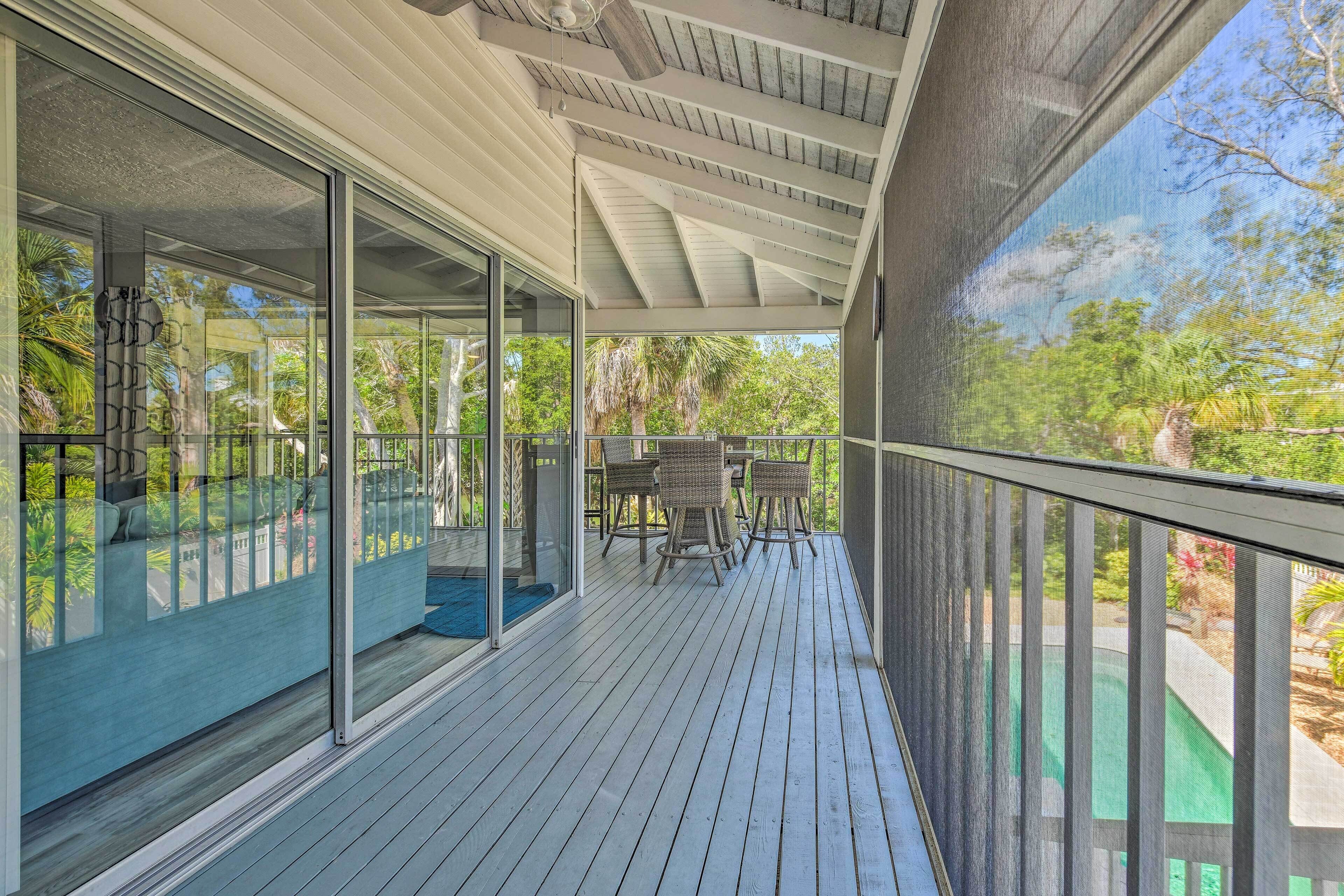Una terraza exterior techada con puertas de cristal que dan a una habitación, un área de comedor con sillas y vistas a zonas verdes.