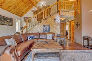 A spacious living room with a large leather sectional sofa, a wooden coffee table, and a staircase with a wooden railing. - Tranquil Ruidoso Cabin w/ Private Hot Tub! (Ruidoso)