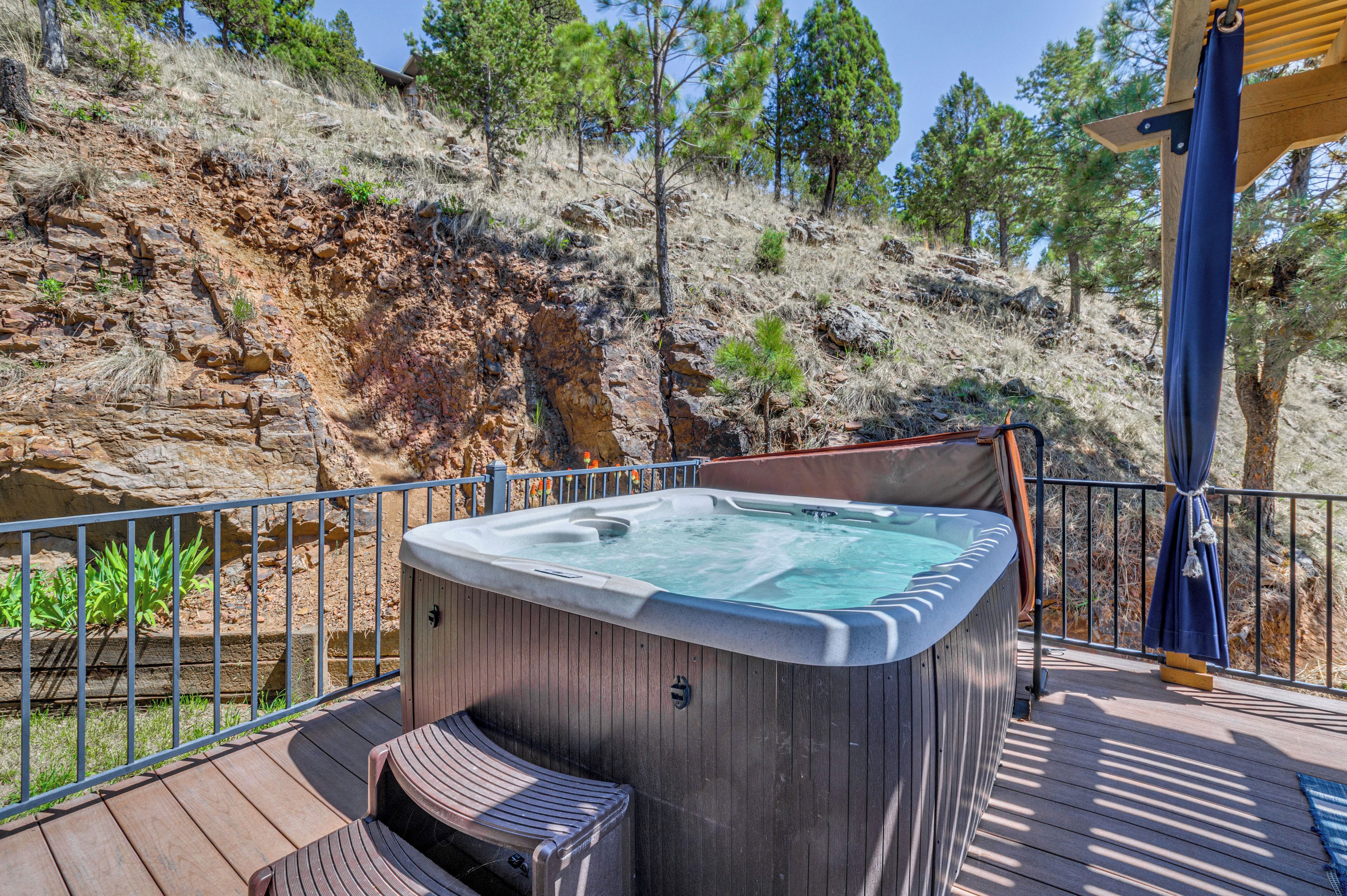 Un bain à remous sur une terrasse en bois, avec vue sur une colline rocheuse et des arbres.