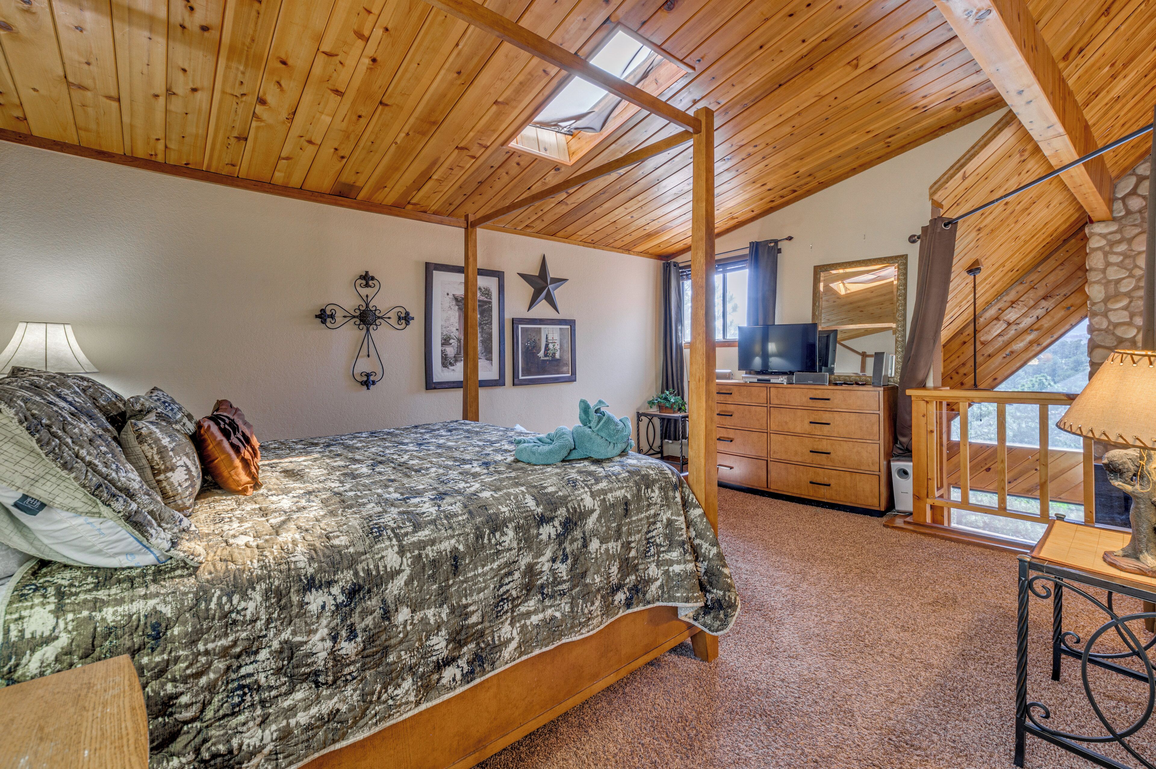 A bedroom with a wooden ceiling, a four-poster bed, a dresser, and a television.