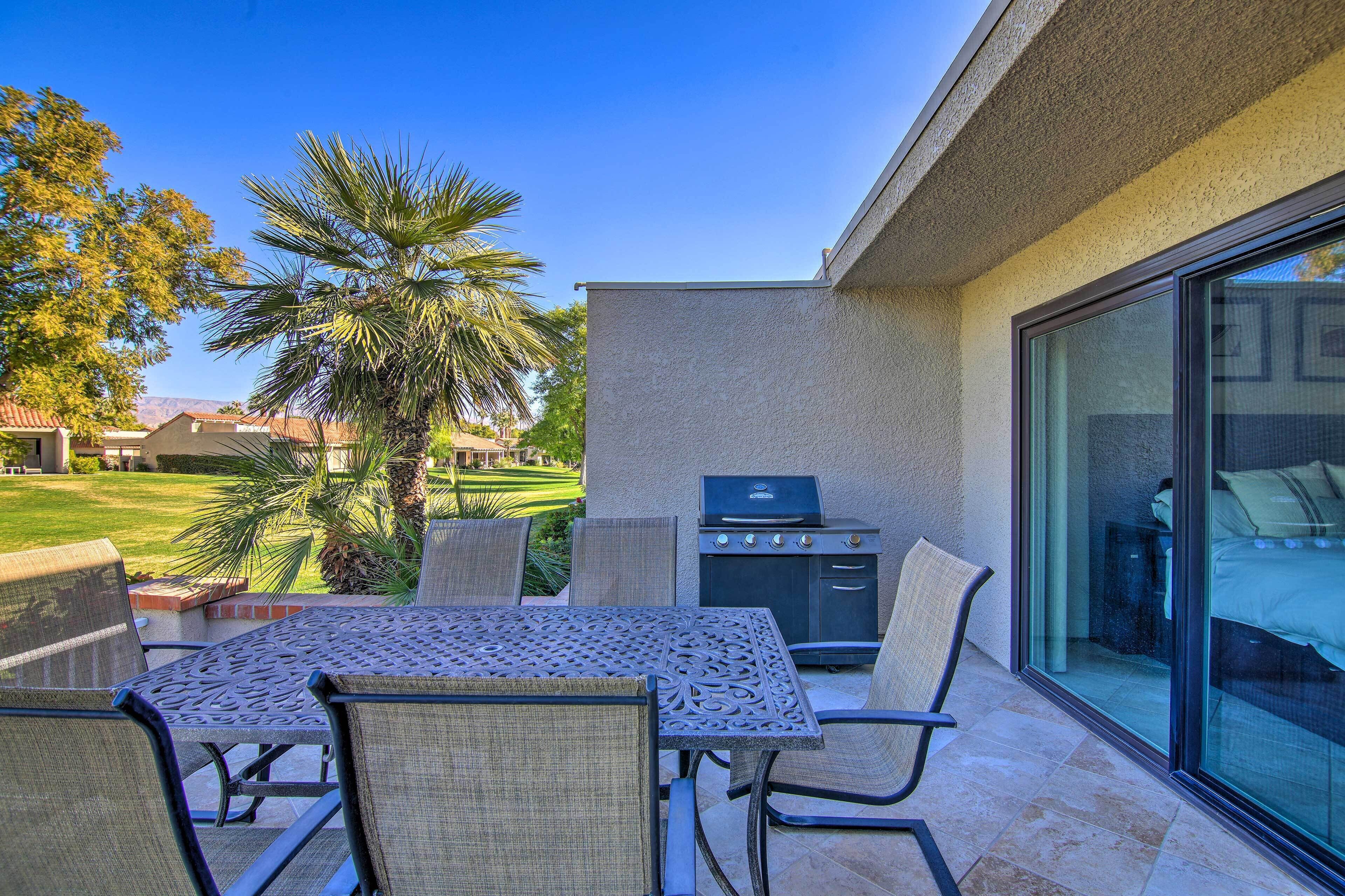 An outdoor patio with a table and chairs, a grill, and a view of a golf course.