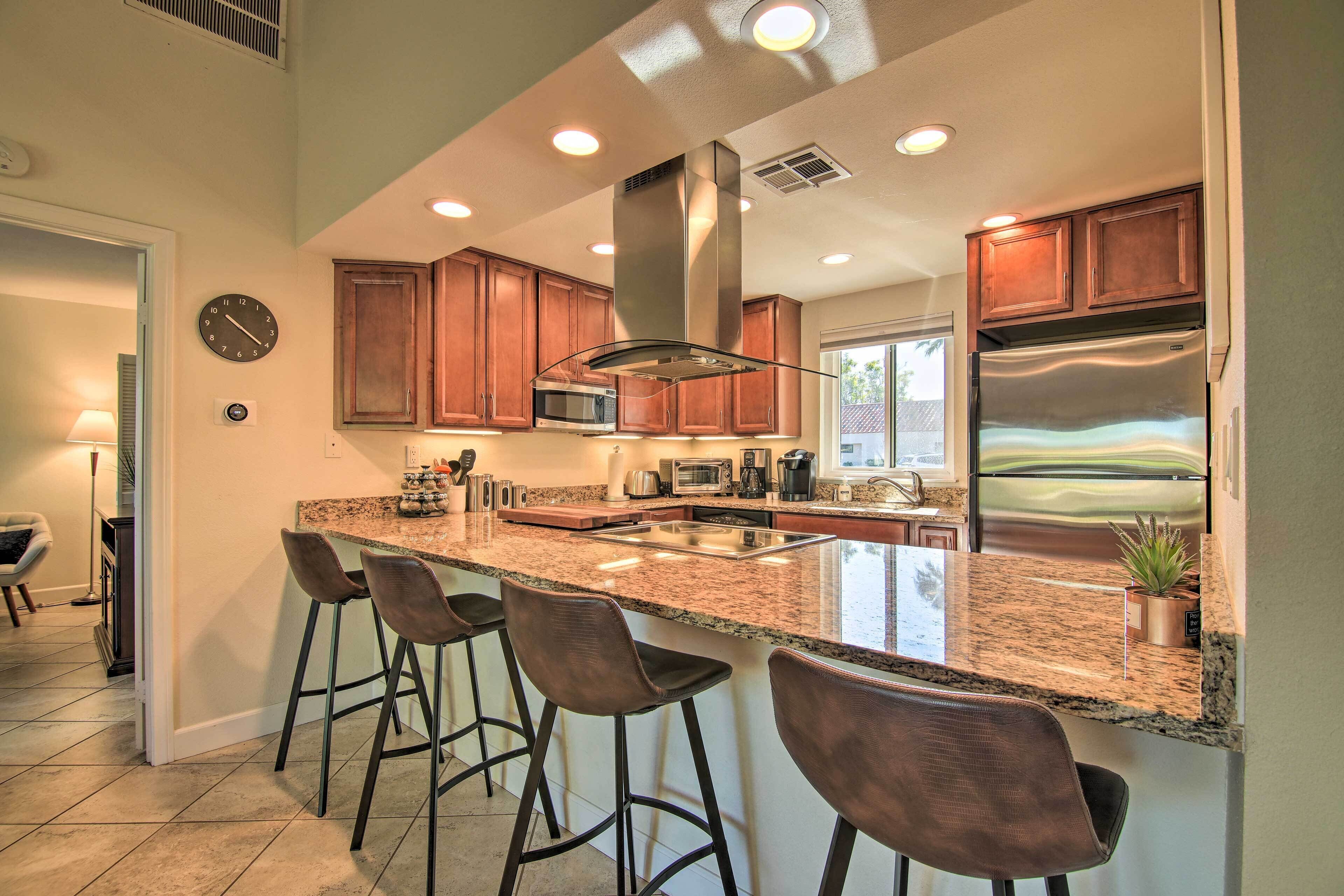 A kitchen with a central island, bar stools, stainless steel appliances, and wooden cabinets.