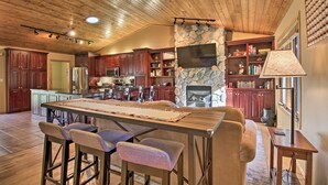 A spacious kitchen with a stone fireplace, wooden ceiling, and a large island with bar stools. - Cabin w/ Fire Pit & Movie Room, 1 Mi to Lake (Pequot Lakes)