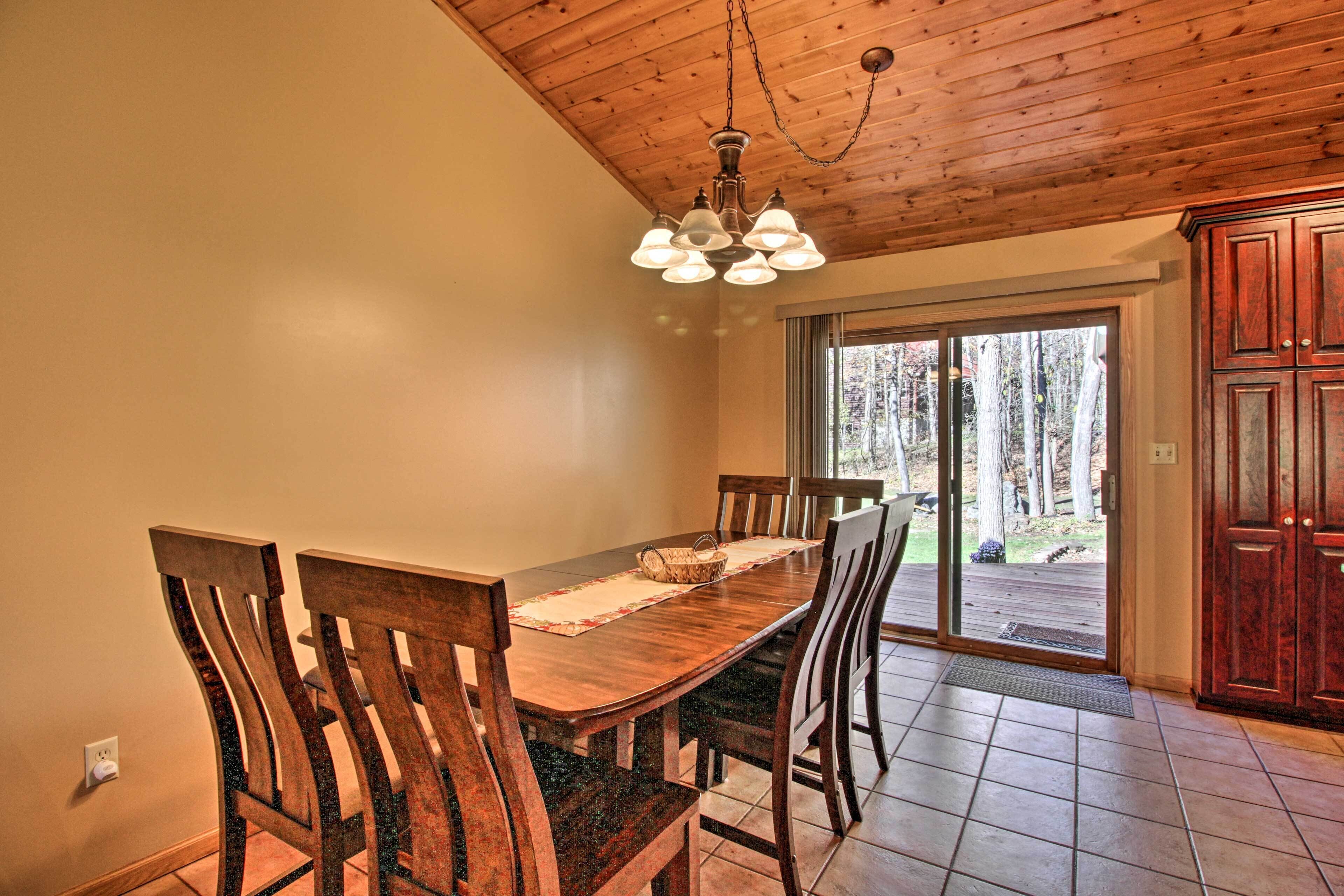 Un coin repas avec une table et des chaises en bois, un lustre et une vue sur l’extérieur grâce à des portes vitrées.