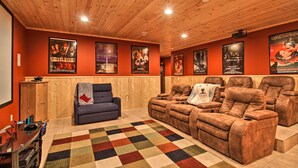 A home theater with wooden paneling, reclining leather chairs, a blue armchair, a multicolored rug, and movie posters on the walls. - Cabin w/ Fire Pit & Movie Room, 1 Mi to Lake (Pequot Lakes)