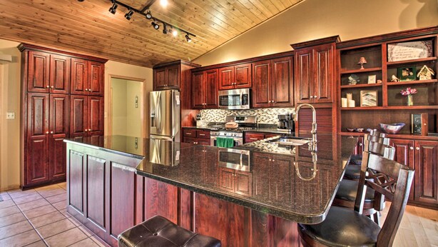 A kitchen with wooden cabinets, a stainless steel refrigerator, a microwave, and a large island with bar seating. - Cabin w/ Fire Pit & Movie Room, 1 Mi to Lake (Pequot Lakes)