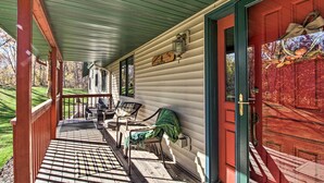 A covered porch with wooden chairs and a bench, a red door, and a sign on the wall. - Cabin w/ Fire Pit & Movie Room, 1 Mi to Lake (Pequot Lakes)