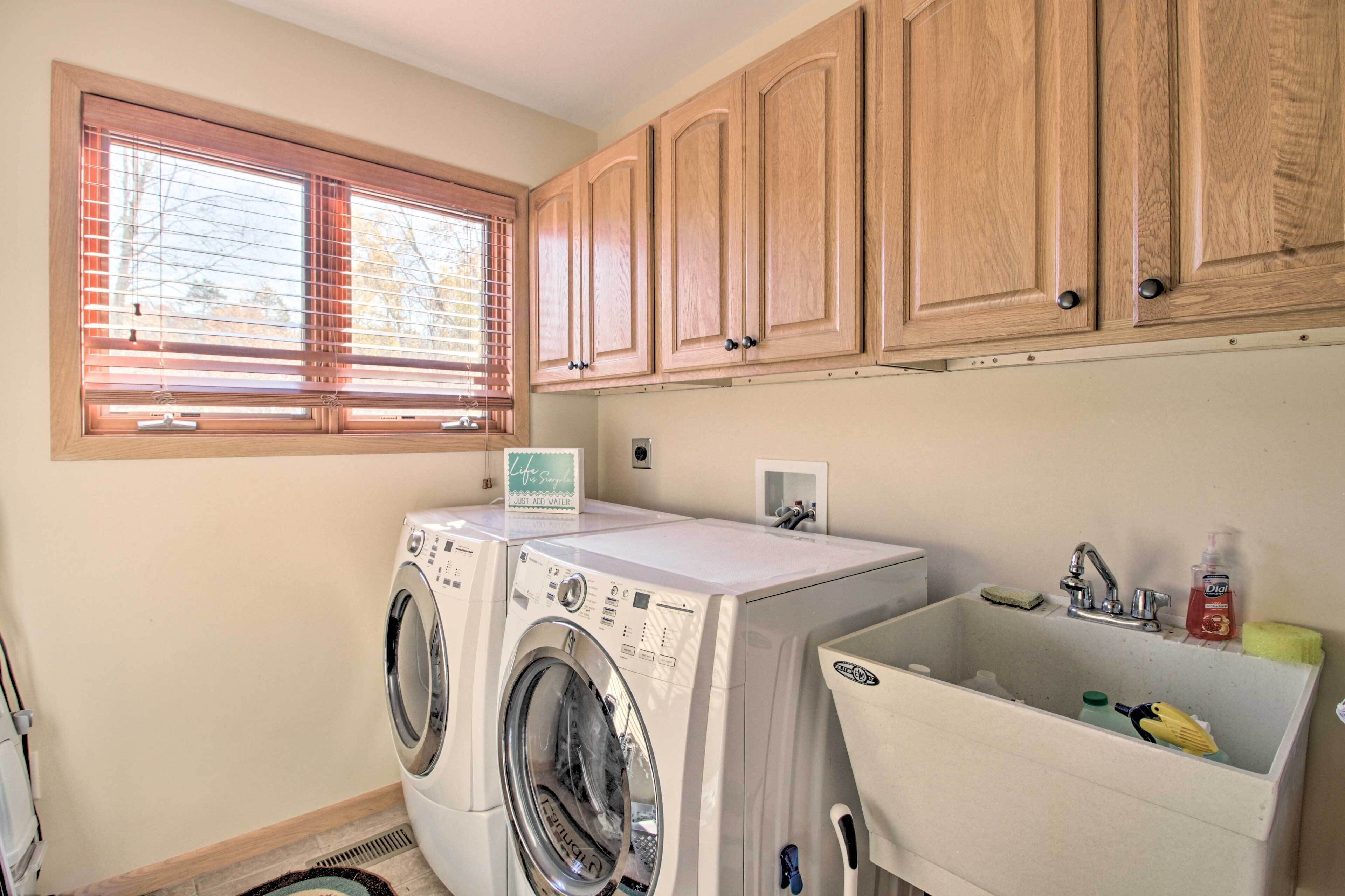 A laundry room with two front-loading washing machines, a sink, wooden cabinets, and a window with blinds.