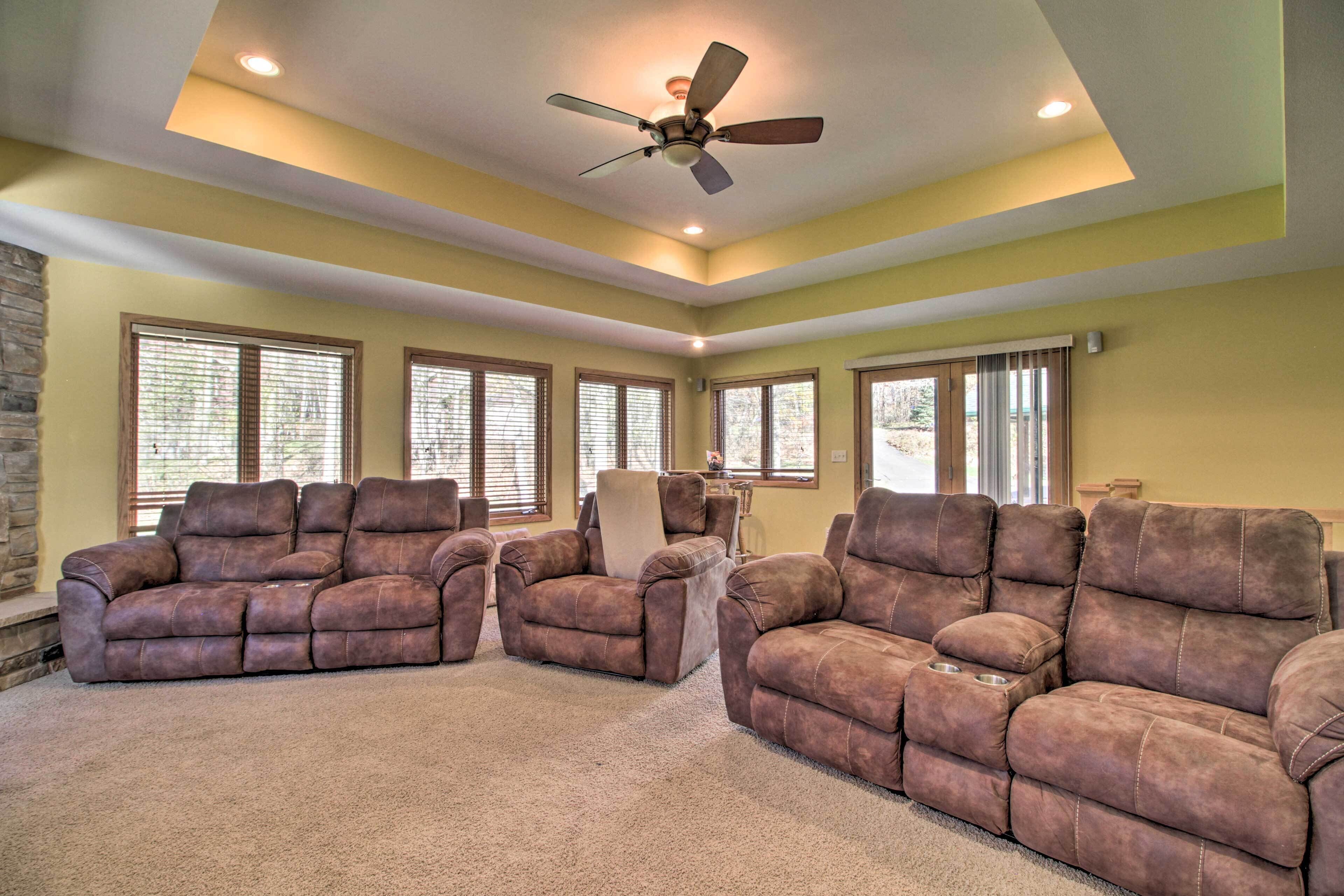 A spacious living room with a ceiling fan, large windows, and a stone fireplace.