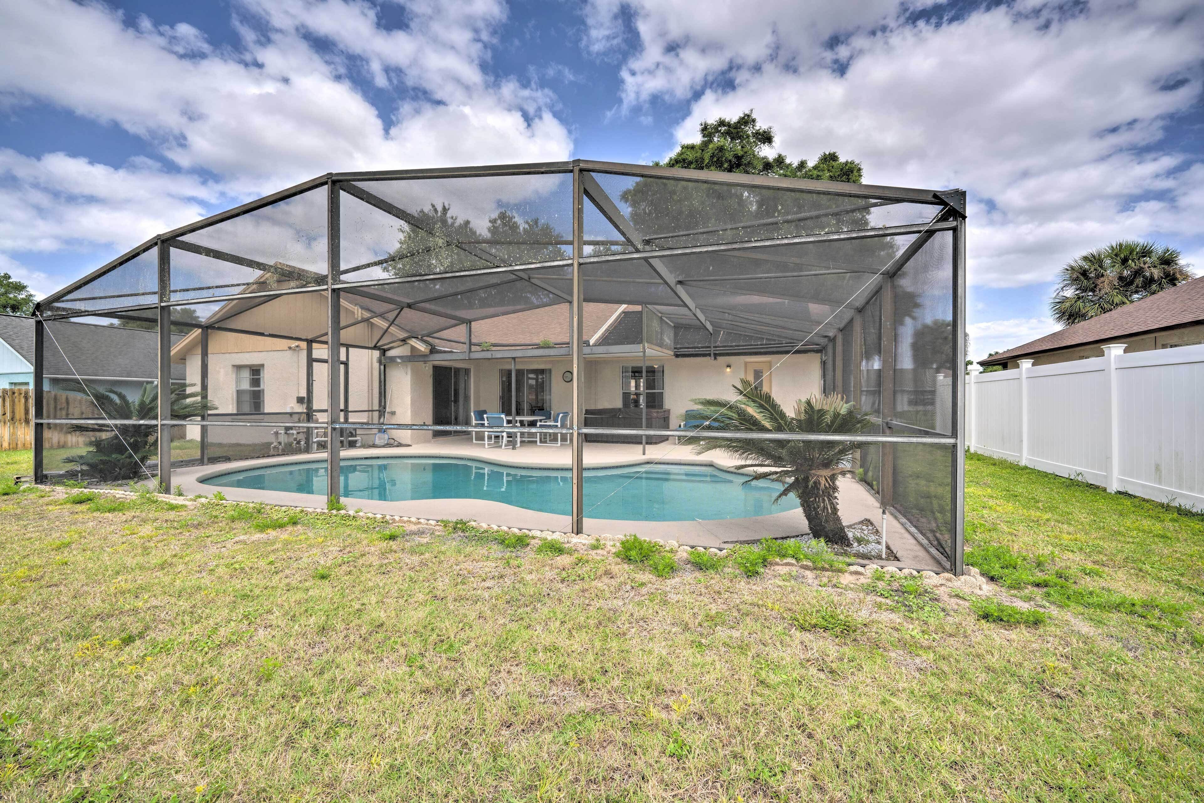 A backyard with a swimming pool, covered patio, and a house in the background.