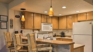 A kitchen with wooden cabinets, a stone countertop, a white refrigerator, and a bar stool area. - Slopeside Condo With Hot Tub + Game Room Access! (Brian Head)