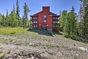 A red multi-story building with balconies, surrounded by a forested area. - Slopeside Condo With Hot Tub + Game Room Access! (Brian Head)