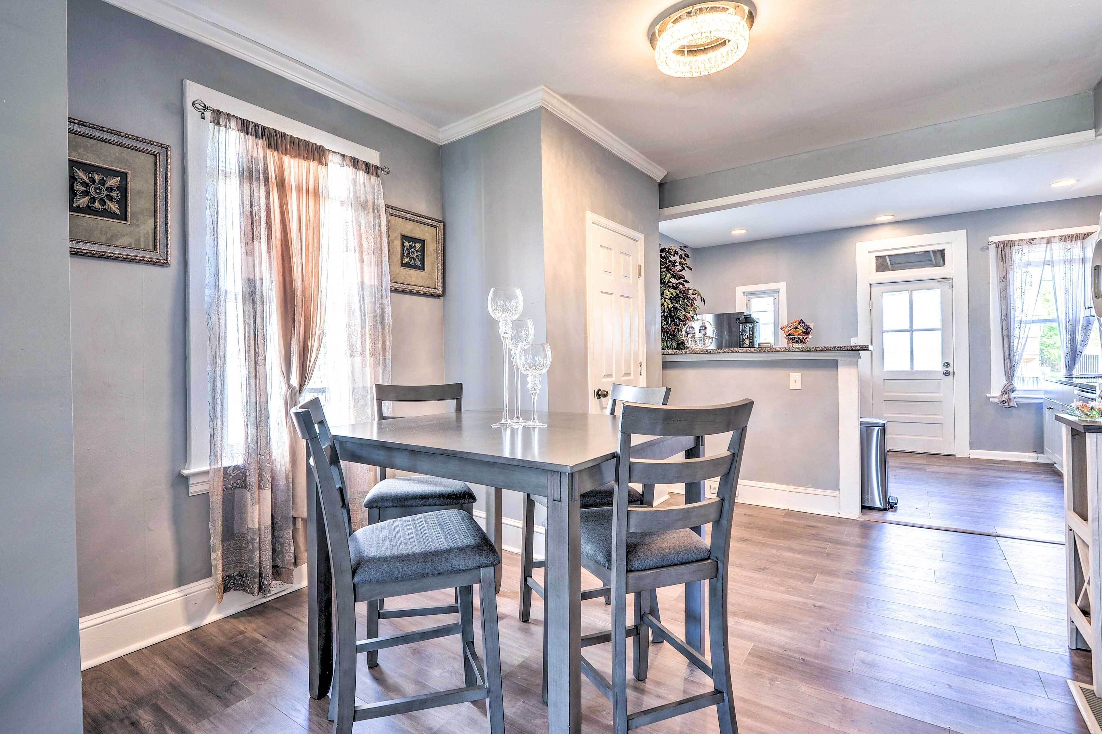 A dining area with a table and chairs, a kitchen in the background, and a hallway leading to another room.