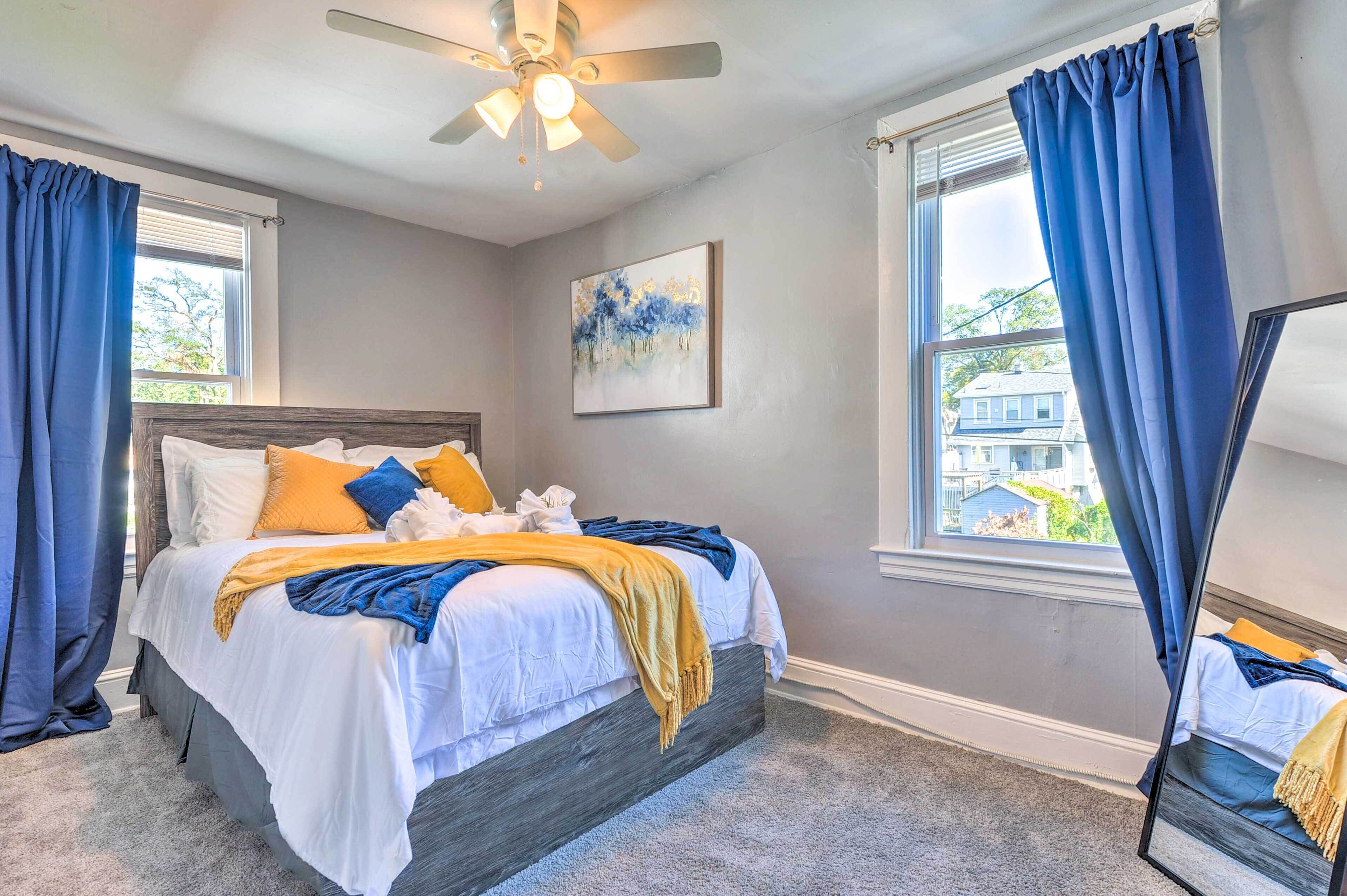 A bedroom with a bed, a ceiling fan, a window with curtains, and a painting on the wall.