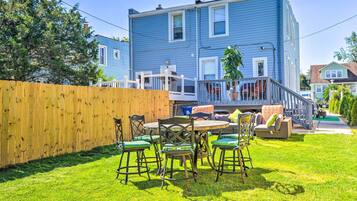 A backyard with a wooden fence, a round table with chairs, and a covered patio area with a sofa and cushions.