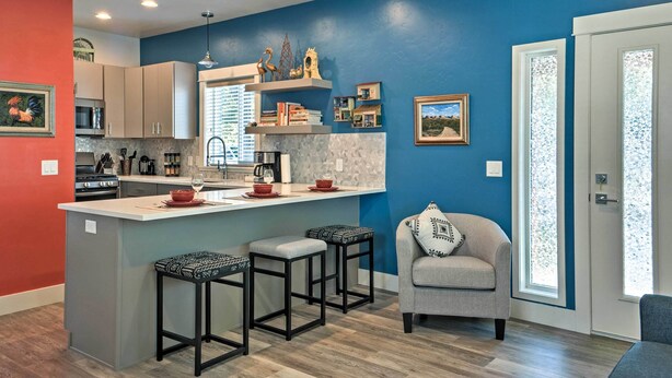 A modern kitchen with a central island, bar stools, and a seating area with a chair and cushions. - Missoula Getaway w/ Balcony, 2 Mi to Downtown! (Missoula)