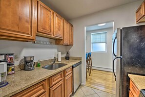 A kitchen with wooden cabinets, a stainless steel refrigerator, a coffee maker, and a dishwasher. - Central & Contemporary NJ Condo: Steps to Shore! (Asbury Park)