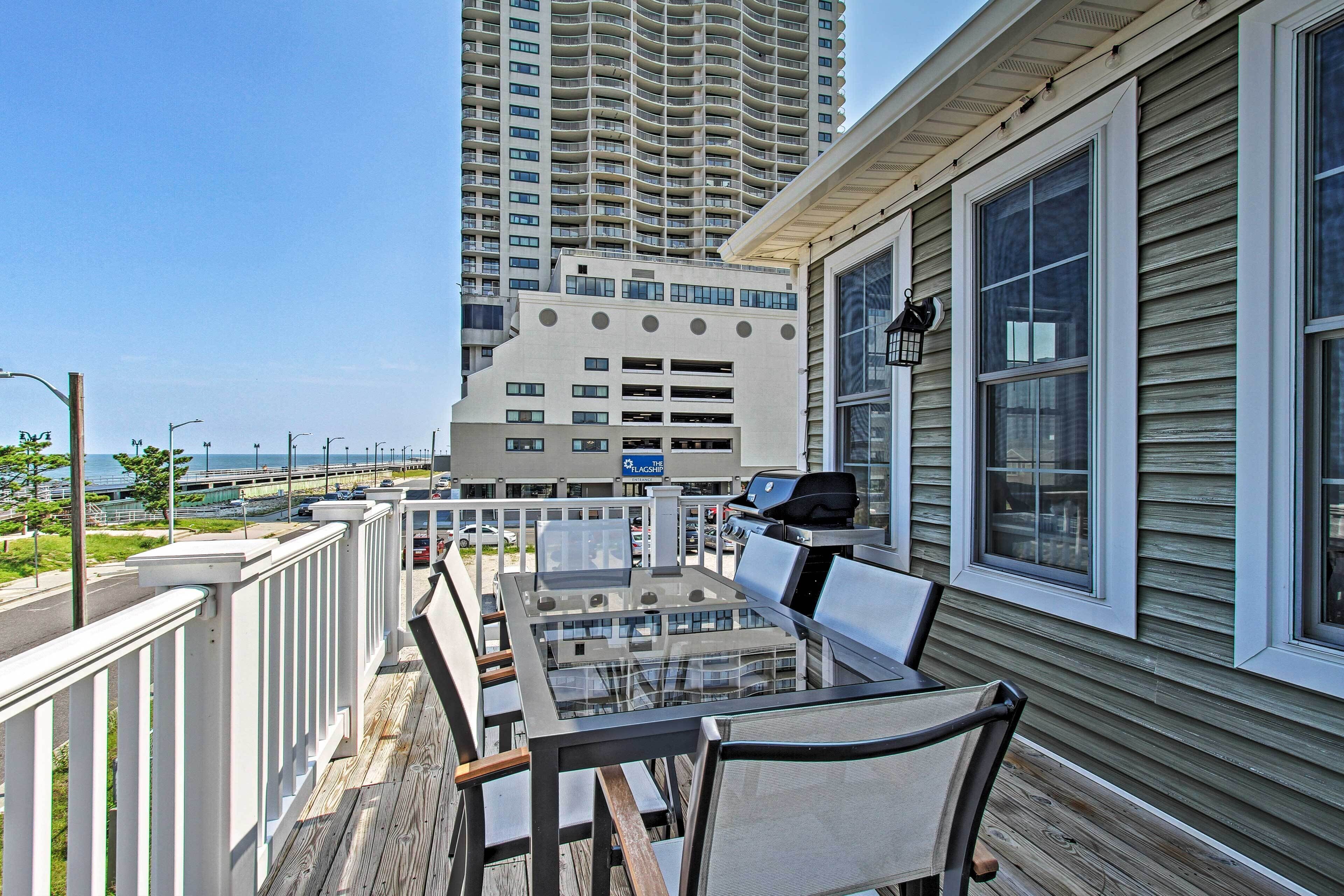 A balcony with a glass-top table and chairs, overlooking a parking garage and a high-rise building.
