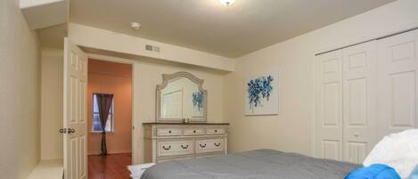 A bedroom with a bed, dresser, and a door leading to another room.