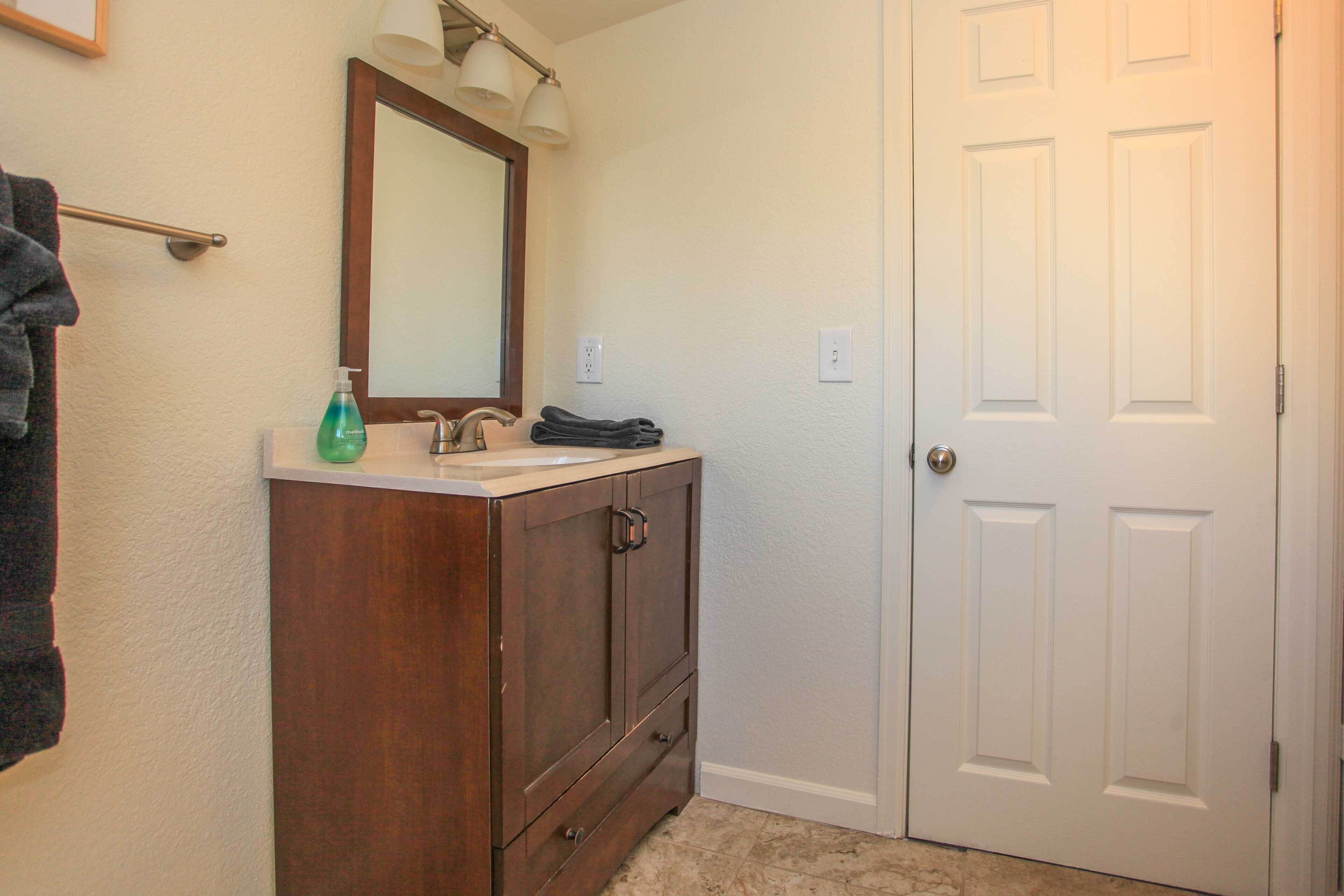 A bathroom with a wooden vanity, a mirror, and a white door.