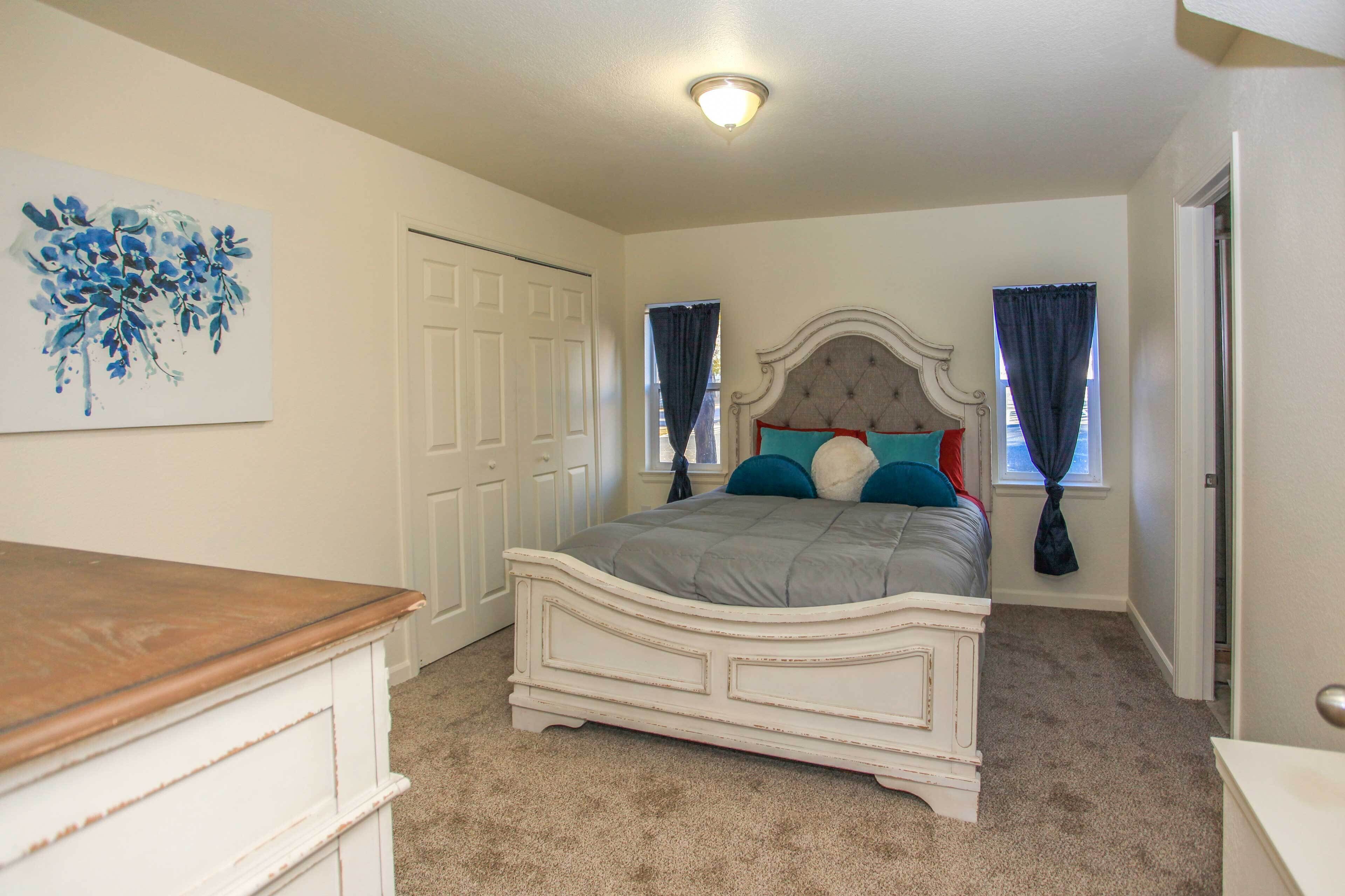 A bedroom with a bed, a dresser, a door, and a painting on the wall.