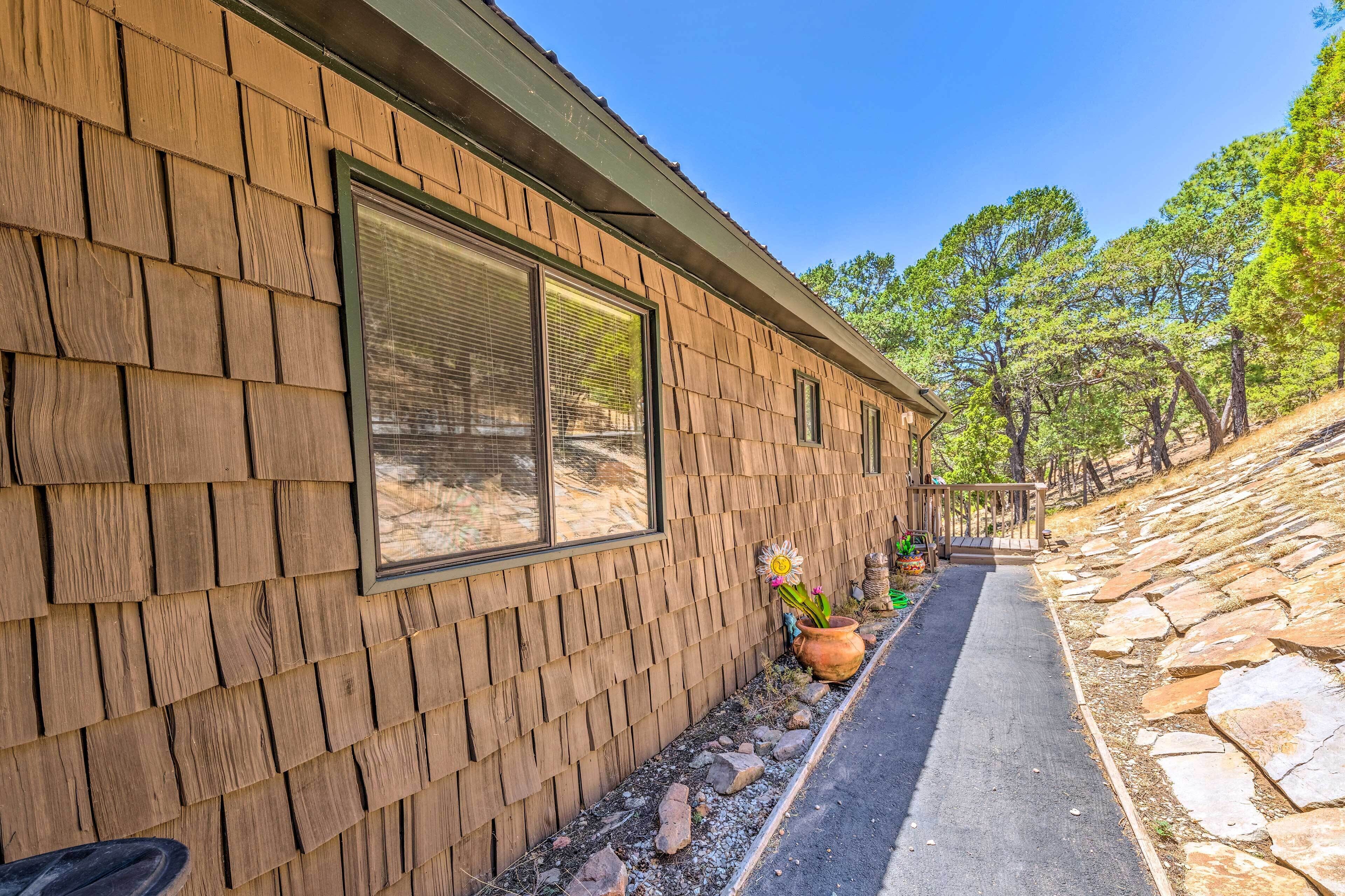 Pared exterior de madera con ventanas amplias, un sendero de piedra y un pequeño jardín con una maceta.