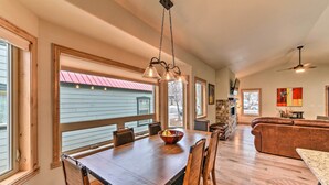 A spacious dining area with a large wooden table and chairs, a stone fireplace, and a view of a red-roofed building through large windows. - Charming Buena Vista Home ~ 1 Block to Main Street (Buena Vista)