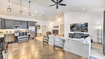 A spacious living area with a large wooden dining table, grey upholstered sofas, and a ceiling fan.