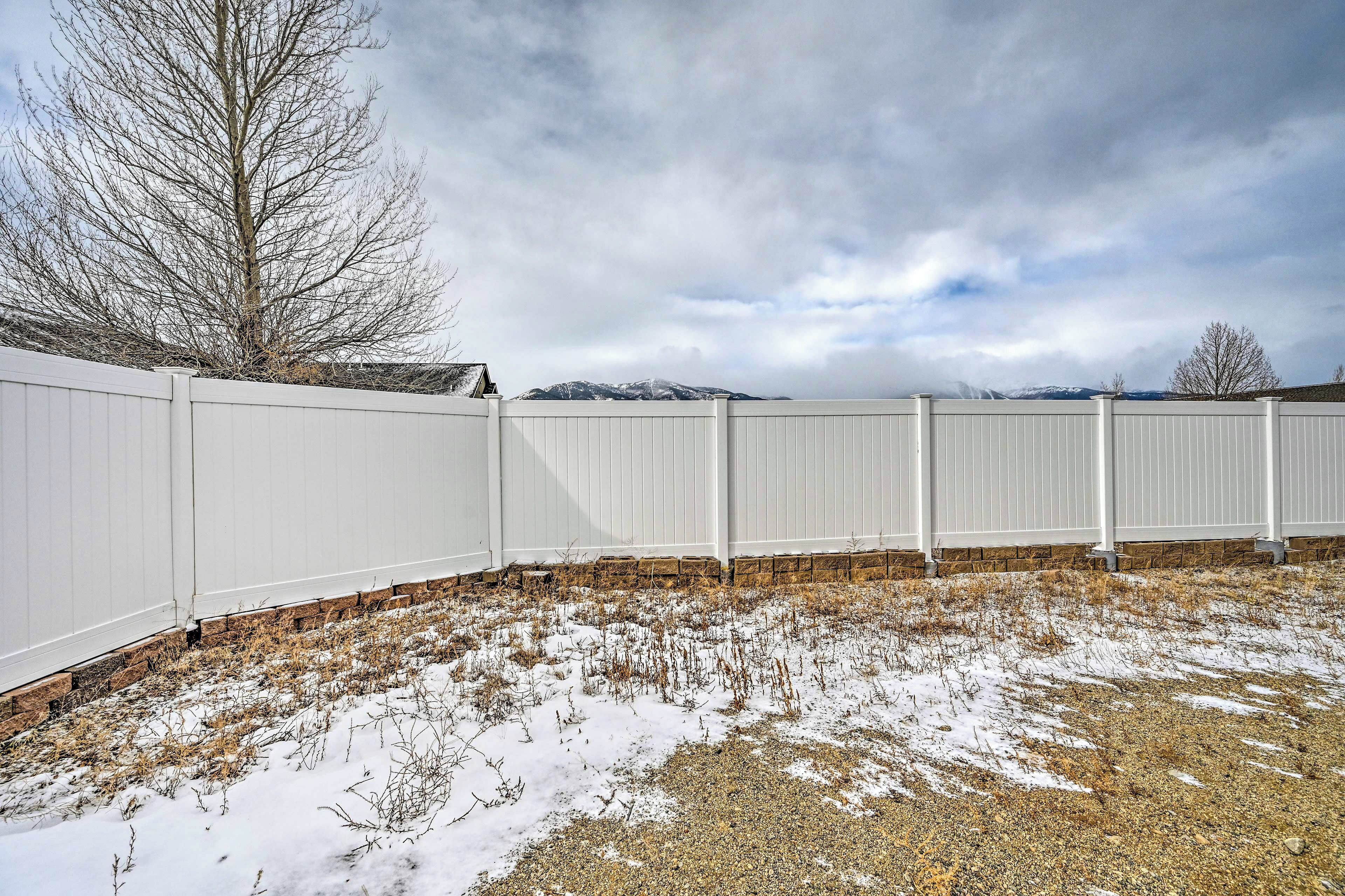 A fenced yard with snow on the ground and a tree in the background.