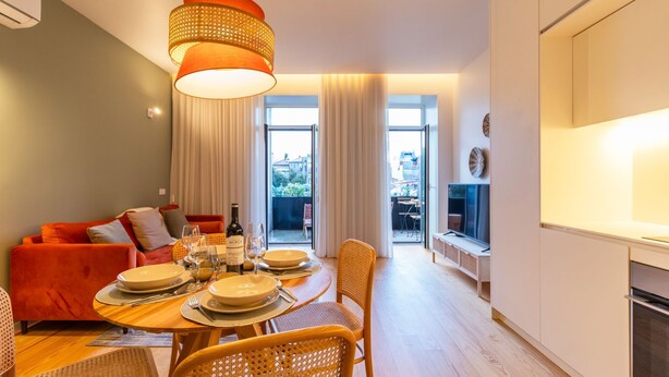 Un salon moderne comprenant un coin repas, un canapé rouge, une table à manger en bois dressée avec des assiettes et des verres, et une grande fenêtre avec des rideaux.