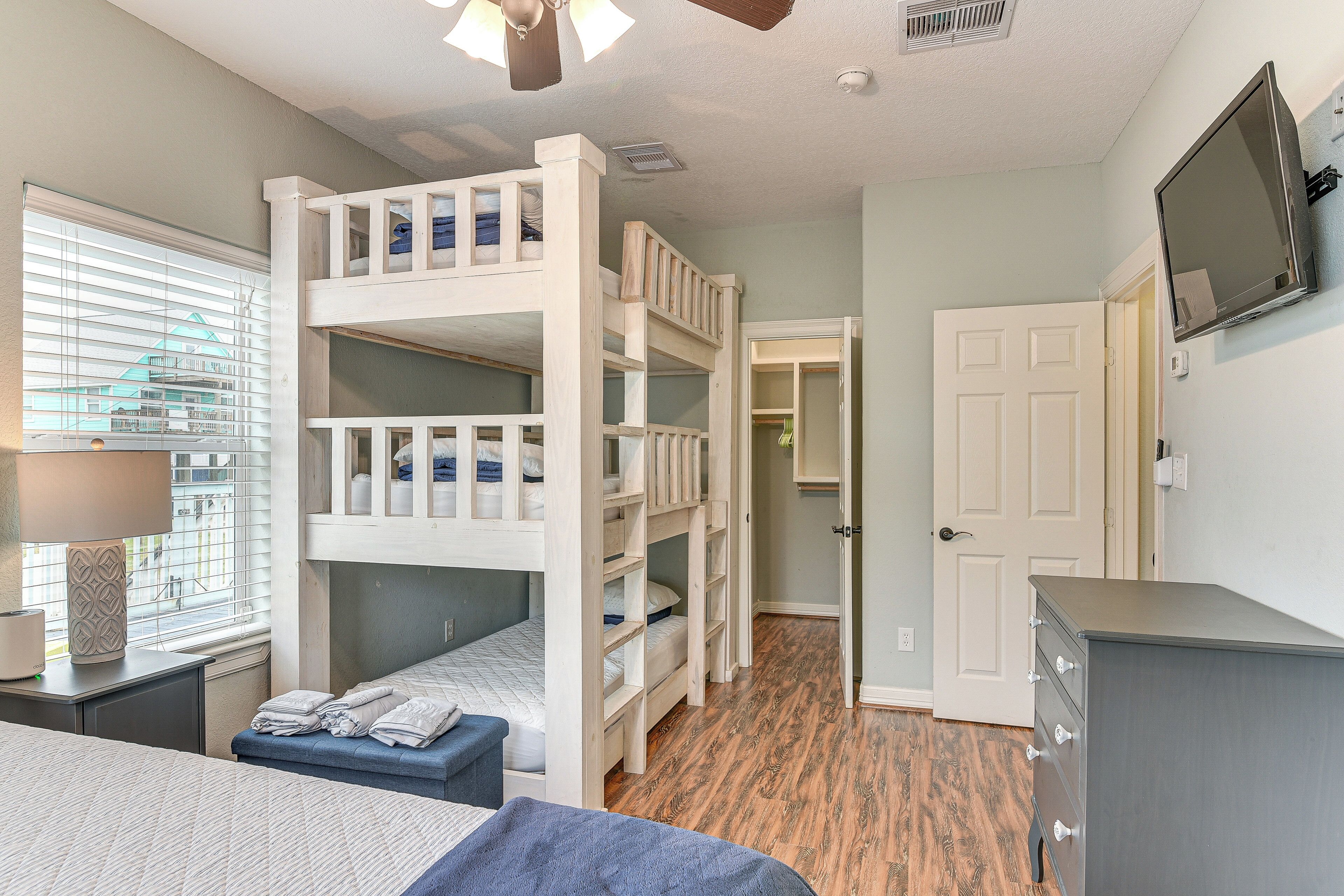 A room with bunk beds, a dresser, a television, and a window with blinds.