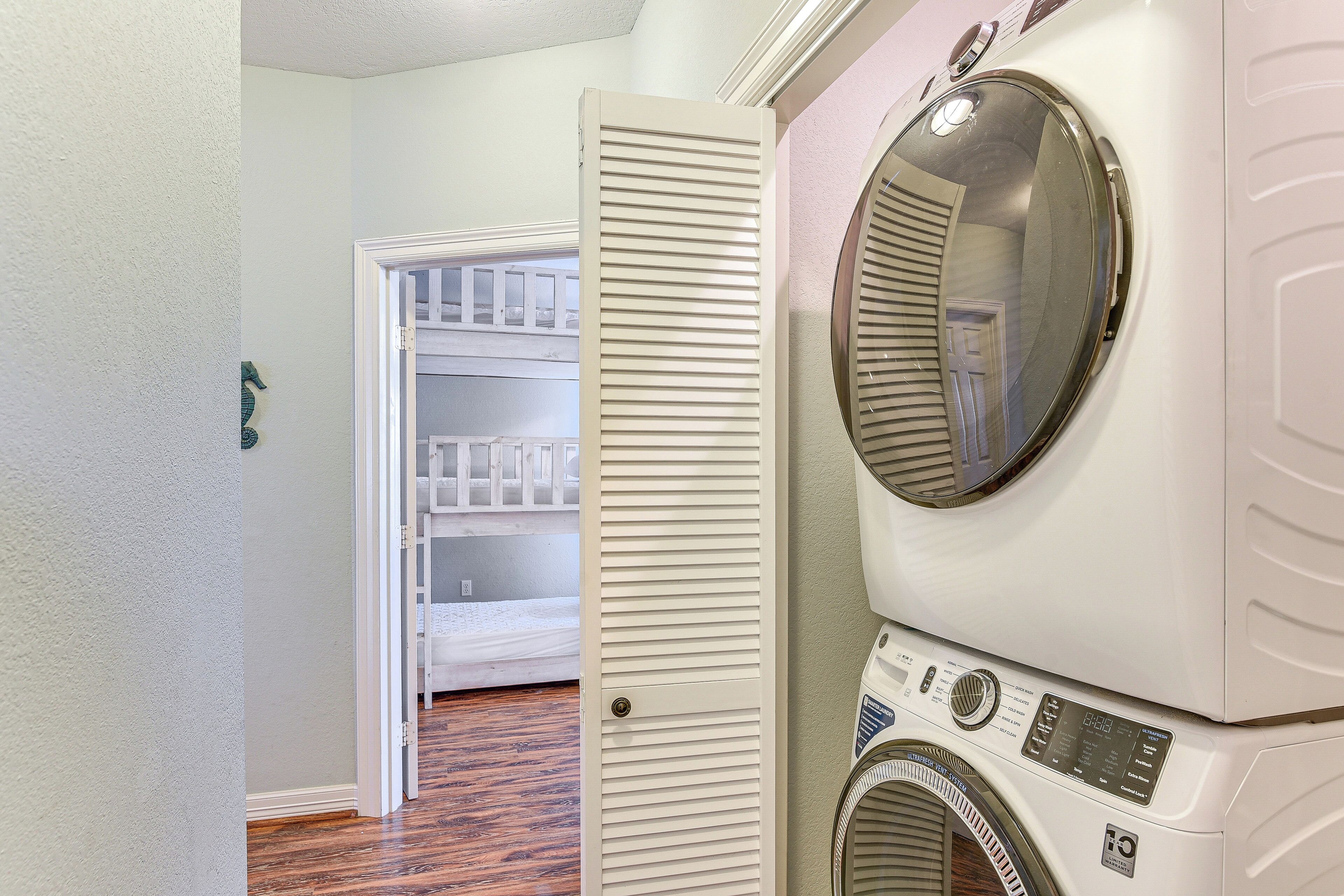 Une buanderie équipée d’un lave-linge et d’un sèche-linge superposés, d’une porte blanche donnant accès à un placard et d’un plancher en bois.