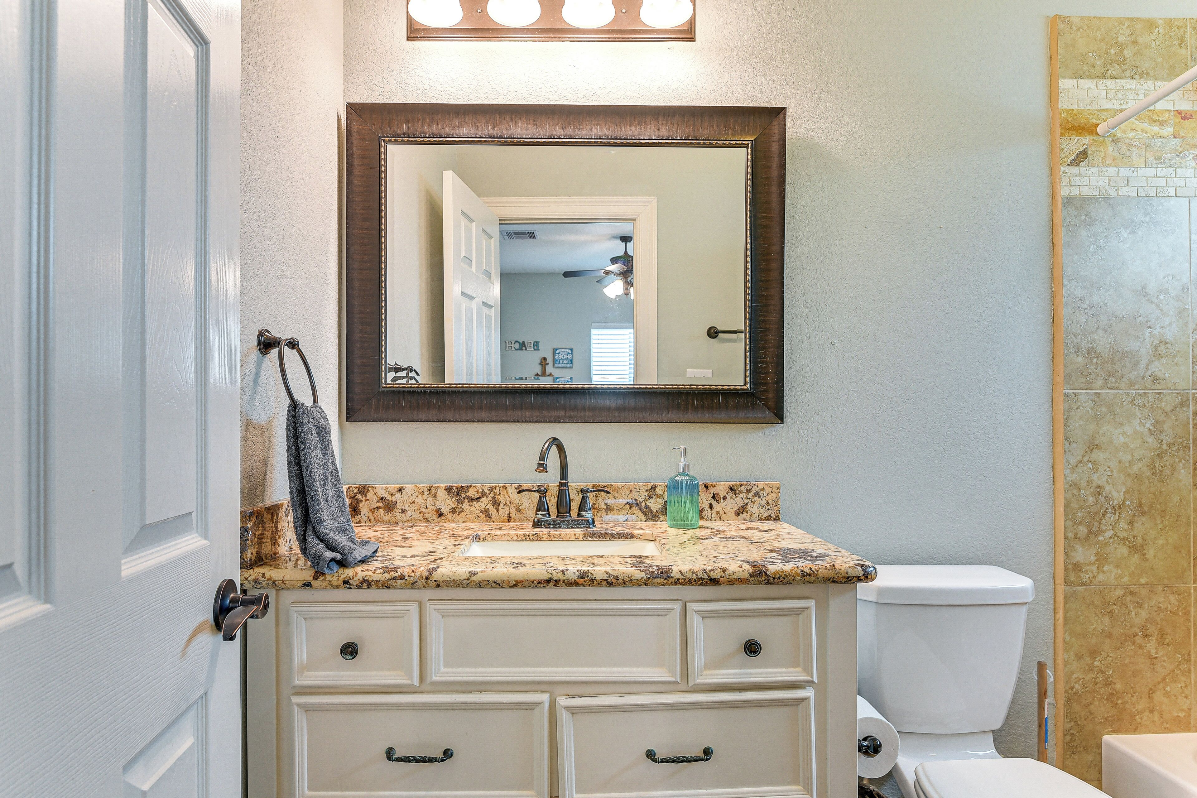 A bathroom with a granite countertop, a white sink, a mirror, and a toilet.