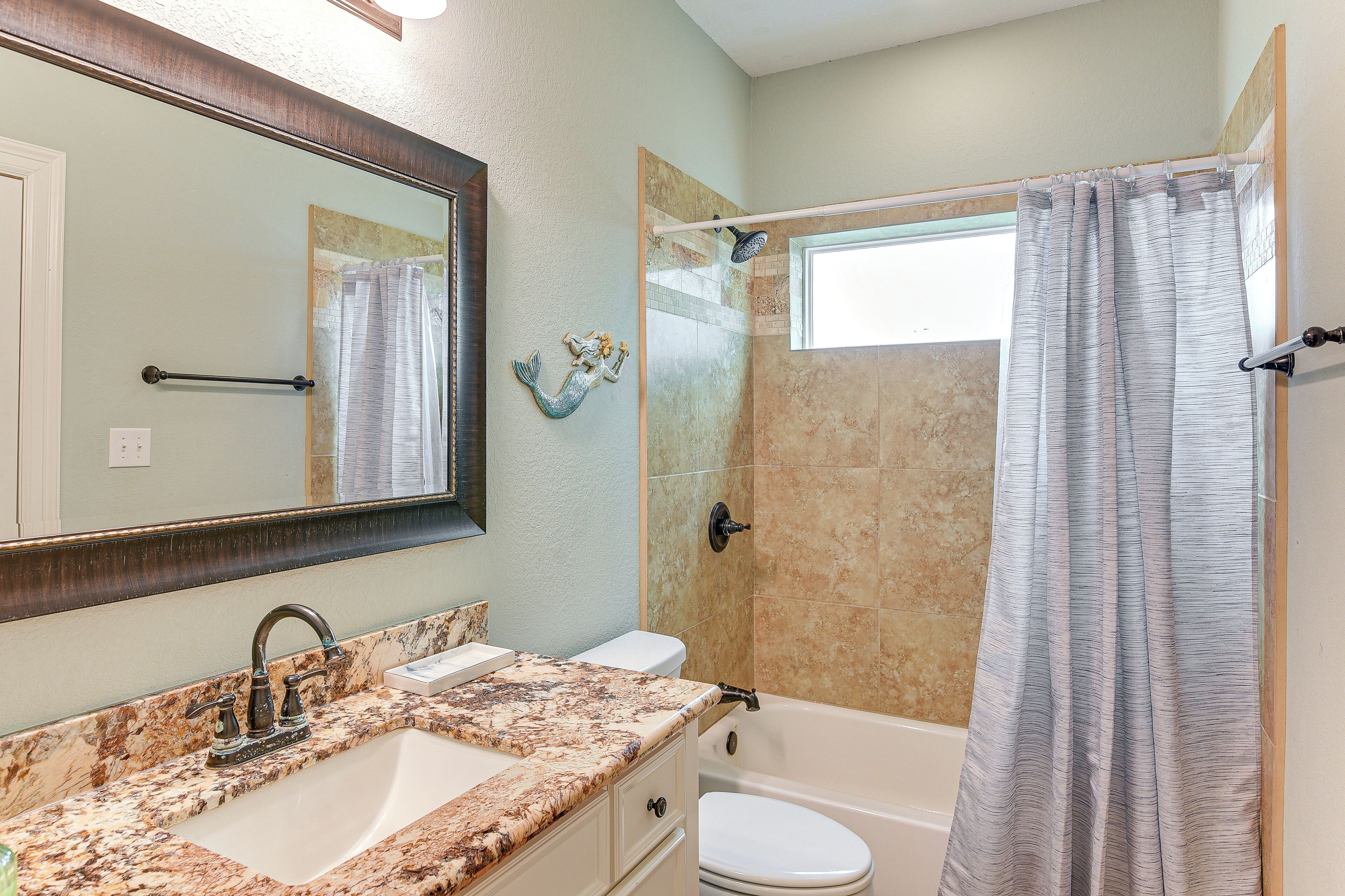 A bathroom with a marble sink, a toilet, a shower with a glass door, and a mirror with a decorative fish.