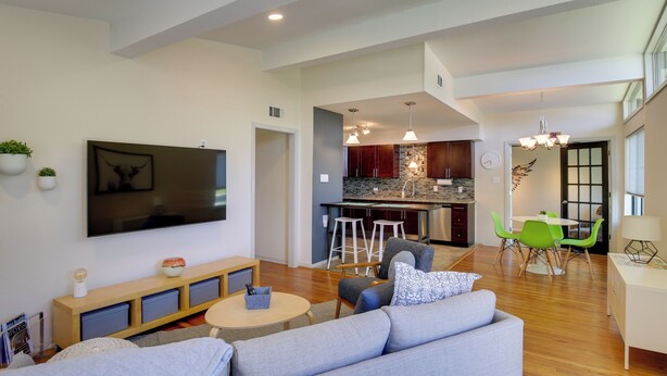 A spacious living room with a large TV, a sofa, a coffee table, and a kitchen area in the background. - Bright & Modern Texas Getaway - 7 Mi to The Alamo! (San Antonio)