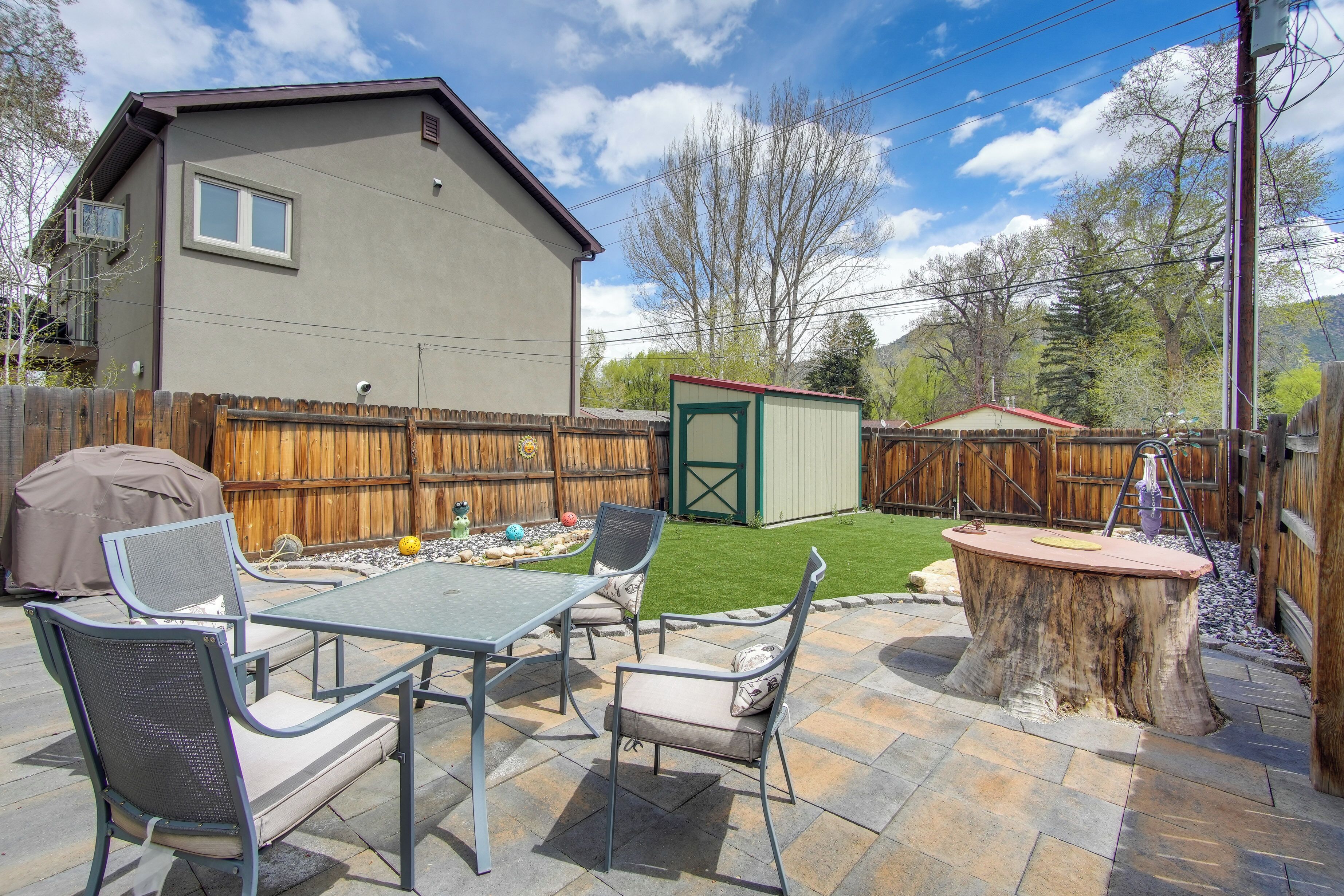 A backyard patio with a table and chairs, a wooden deck, and a shed.