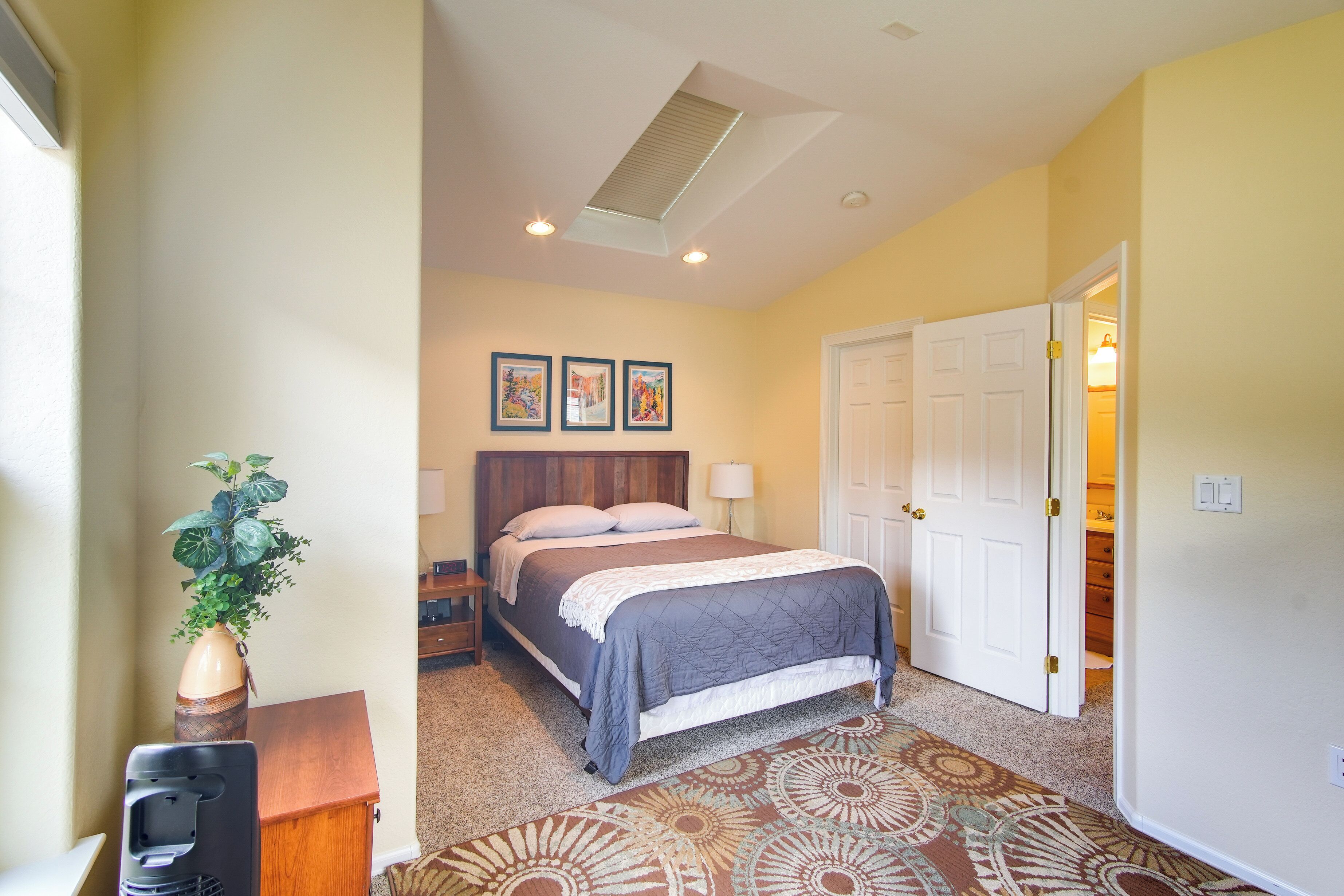 A bedroom with a bed, nightstands, a lamp, a plant, and a door leading to a closet.